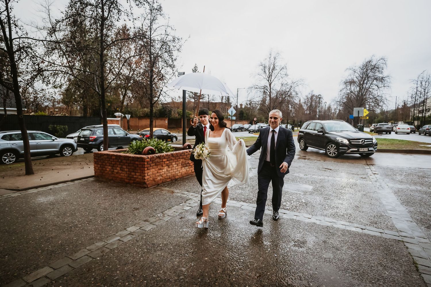 Bride and groom walking hand in hand in the rain on their wedding day in a wet parking lot.