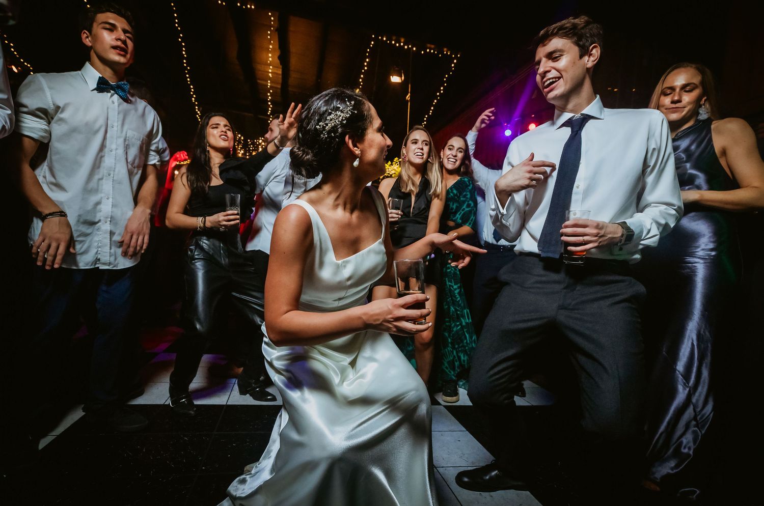 Bride and groom dancing joyfully at wedding reception surrounded by guests on dance floor.