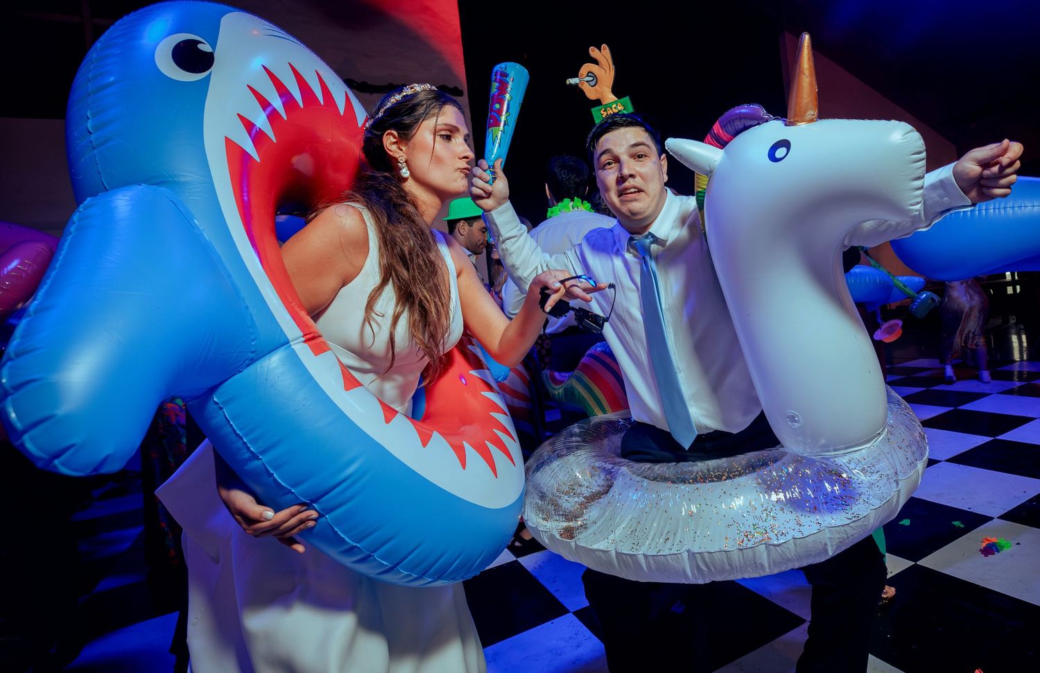Couple celebrating with inflatable shark and unicorn pool floats at wedding.