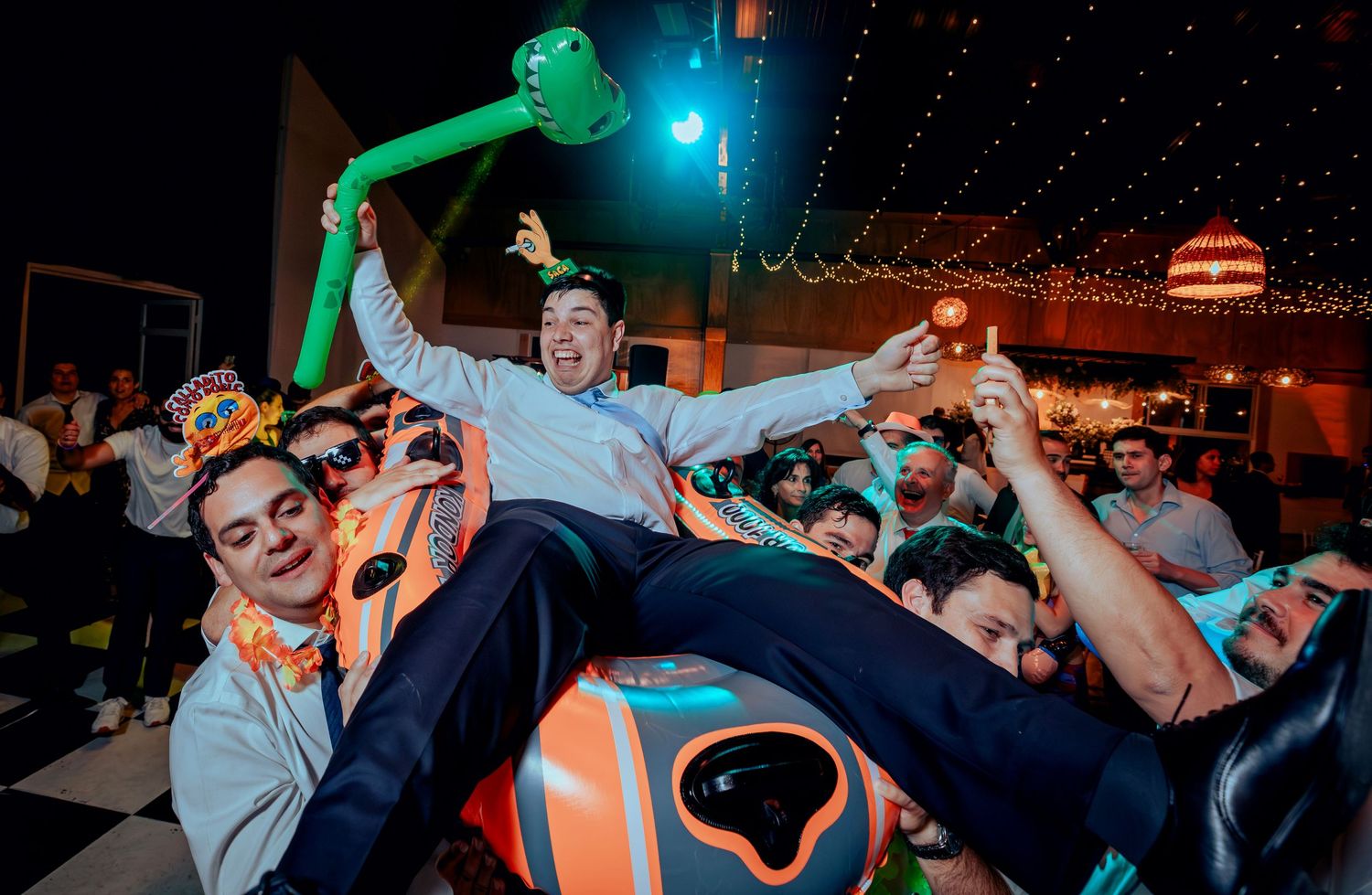 Groom crowd surfing over cheering guests at colorful wedding reception.