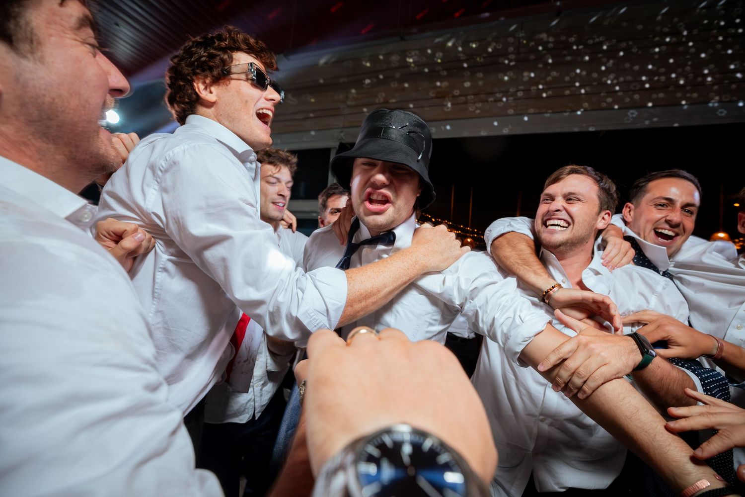 Groomsmen in white shirts laugh and celebrate wildly at wedding reception party.