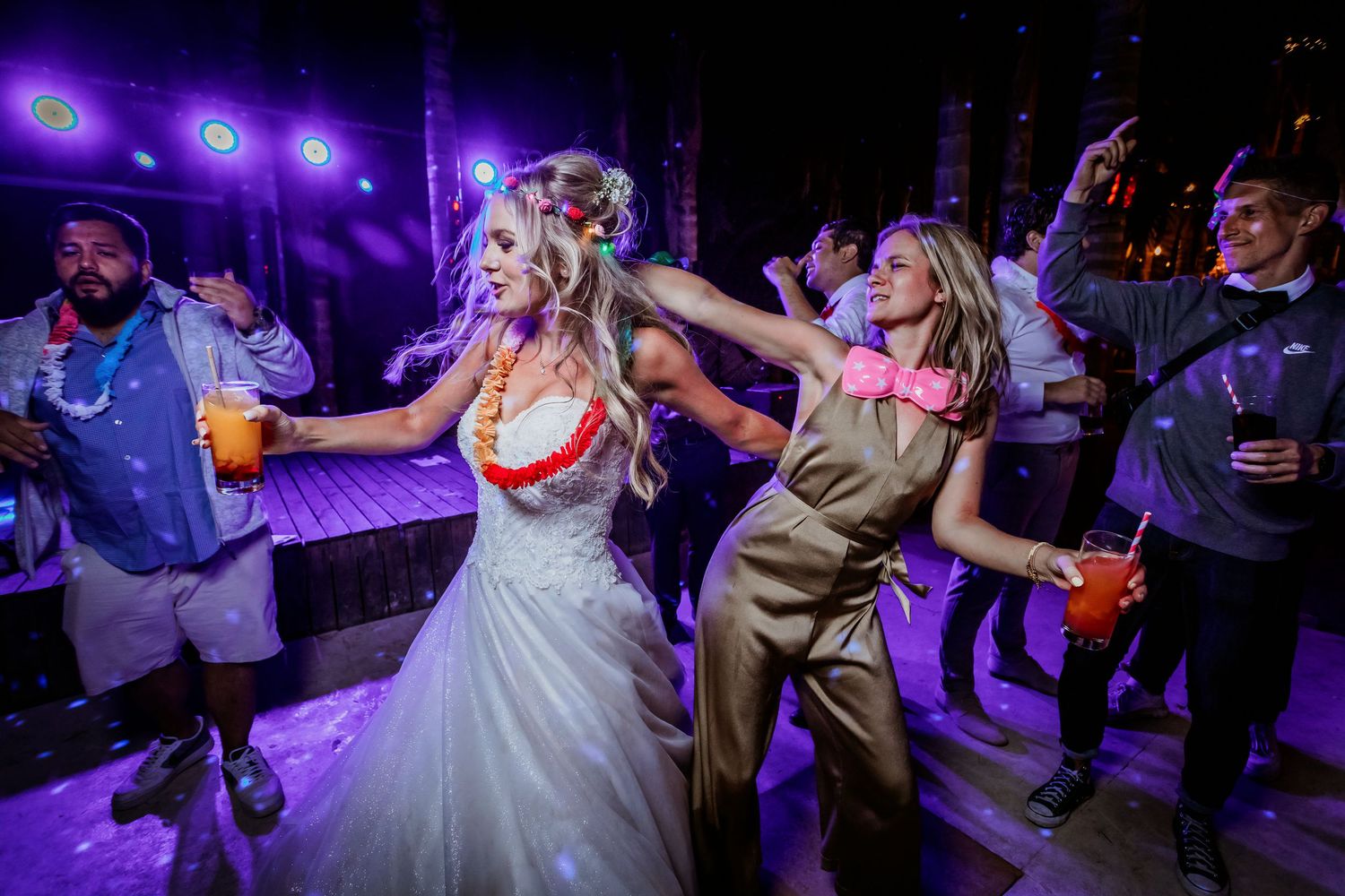 Bride dancing energetically with guests at a vibrant wedding reception under purple lights.