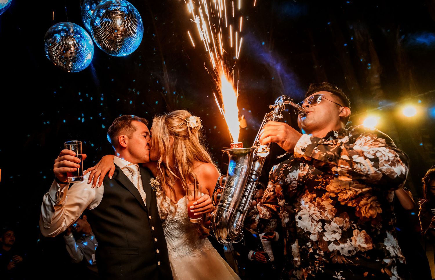 Bride and groom share kiss beside saxophonist with spectacular fireworks display.