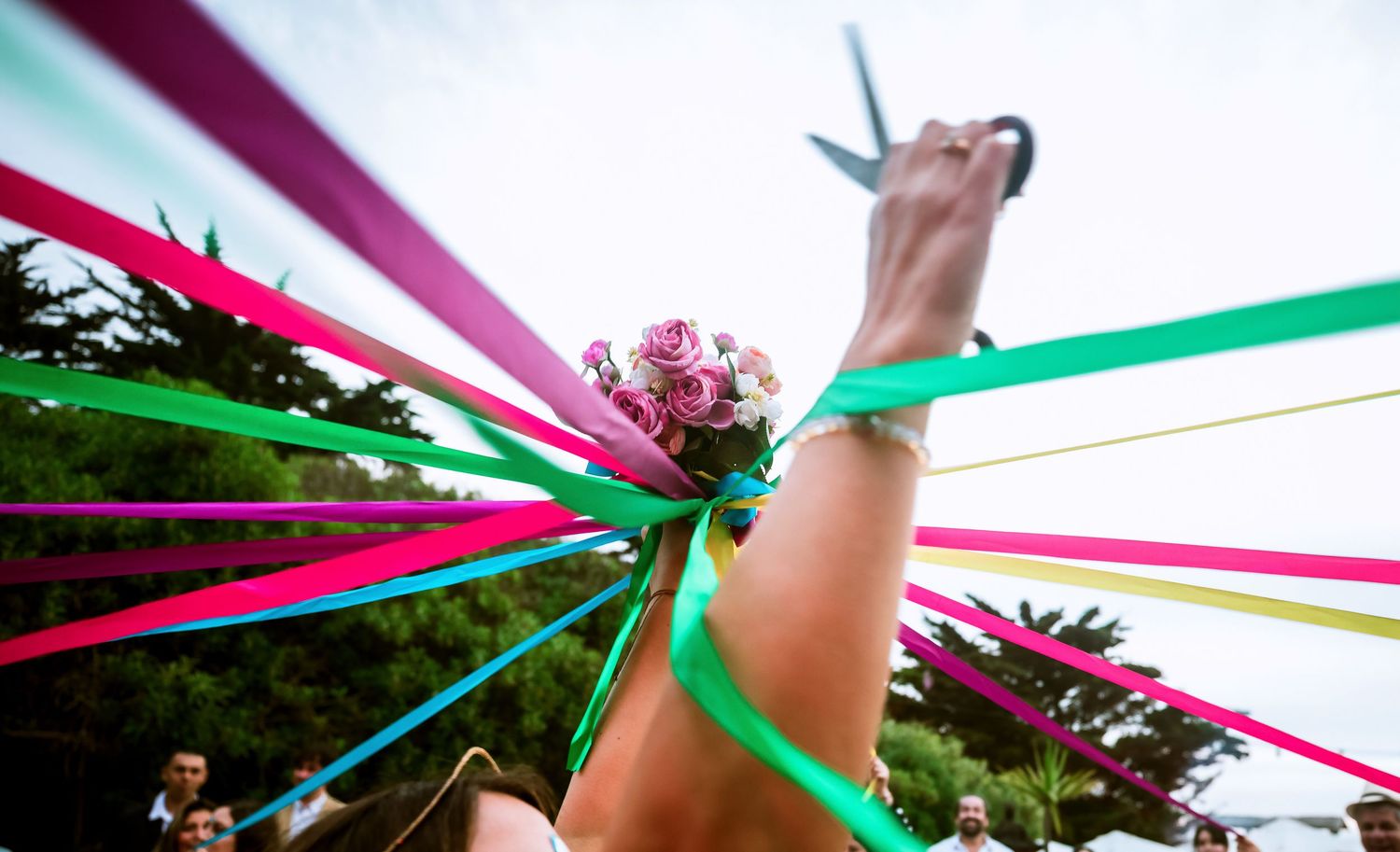 Close-up of bride holding floral bouquet wrapped in vibrant multicolored ribbons at wedding.