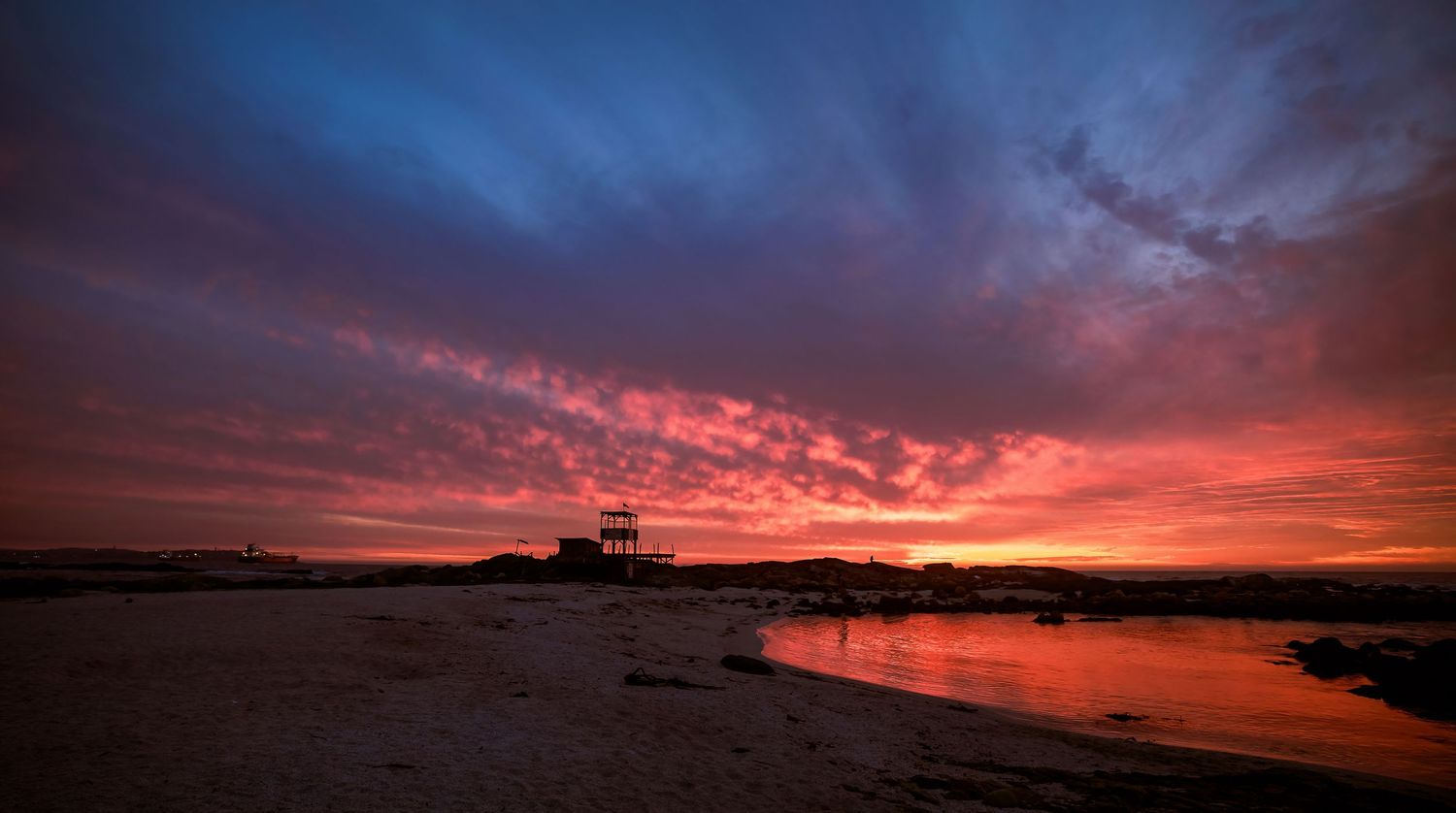 Stunning crimson and blue sunset sky reflecting over calm beach shoreline.
