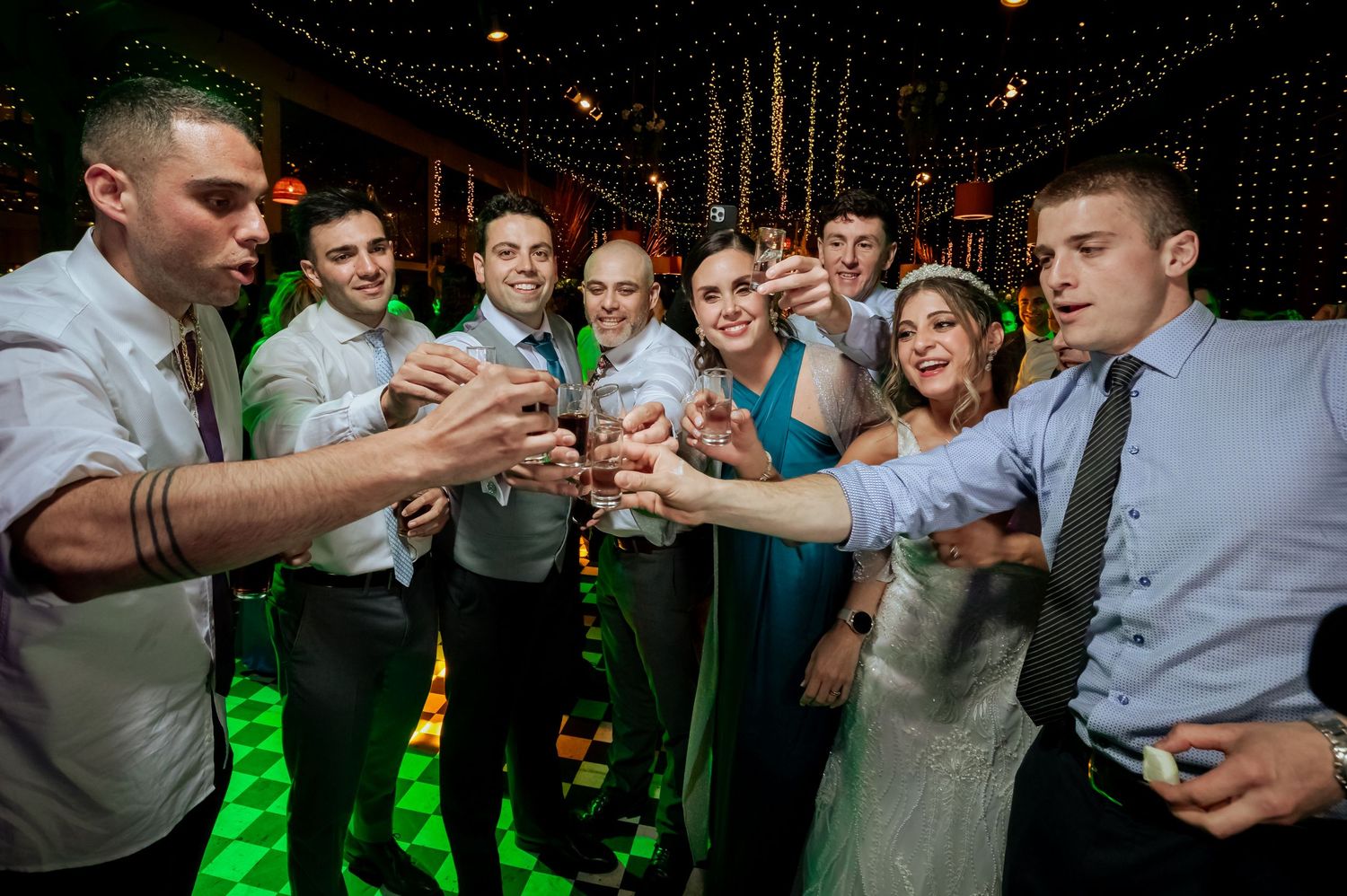 Wedding guests toast and celebrate with the bride in a green-lit reception venue.