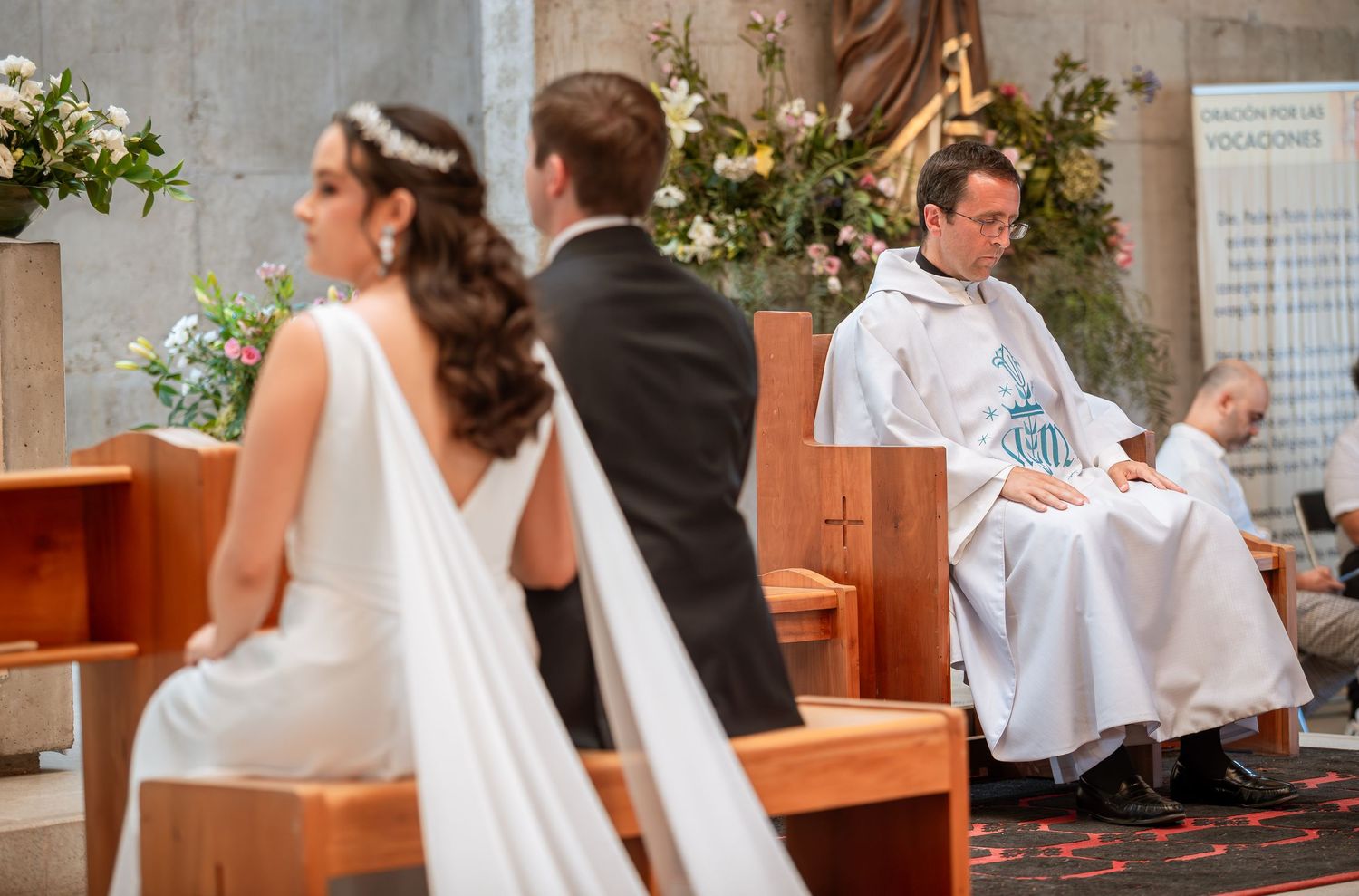 Bride and groom stand before priest during Catholic wedding ceremony in church.