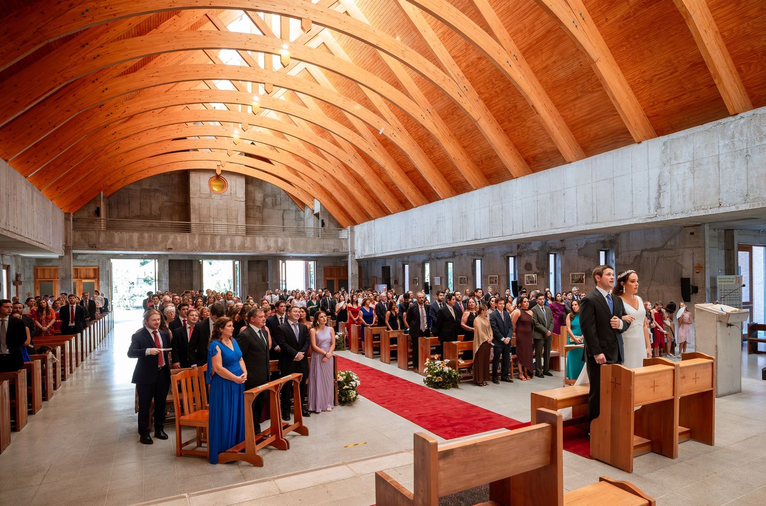 Full church wedding ceremony with guests filling pews under a stunning wooden arched ceiling.