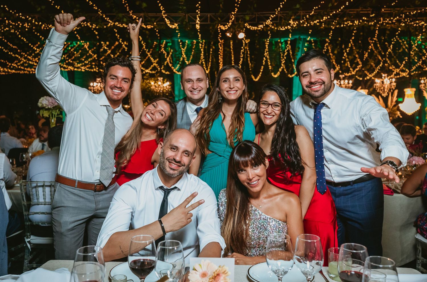 Group of eight friends smiling and posing together at outdoor wedding reception.