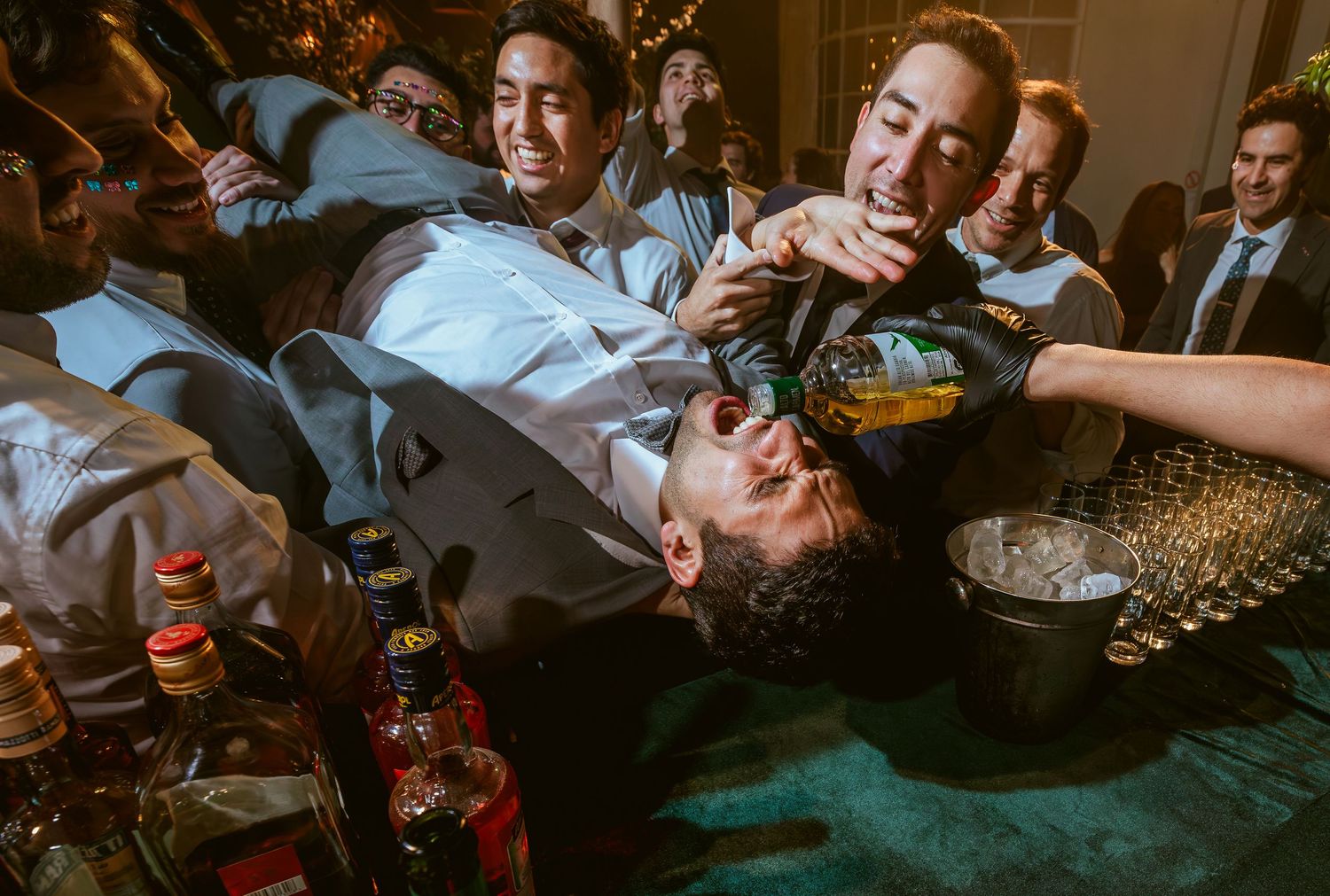 Groomsmen celebrating at a wedding reception, pouring drinks during a lively party moment.
