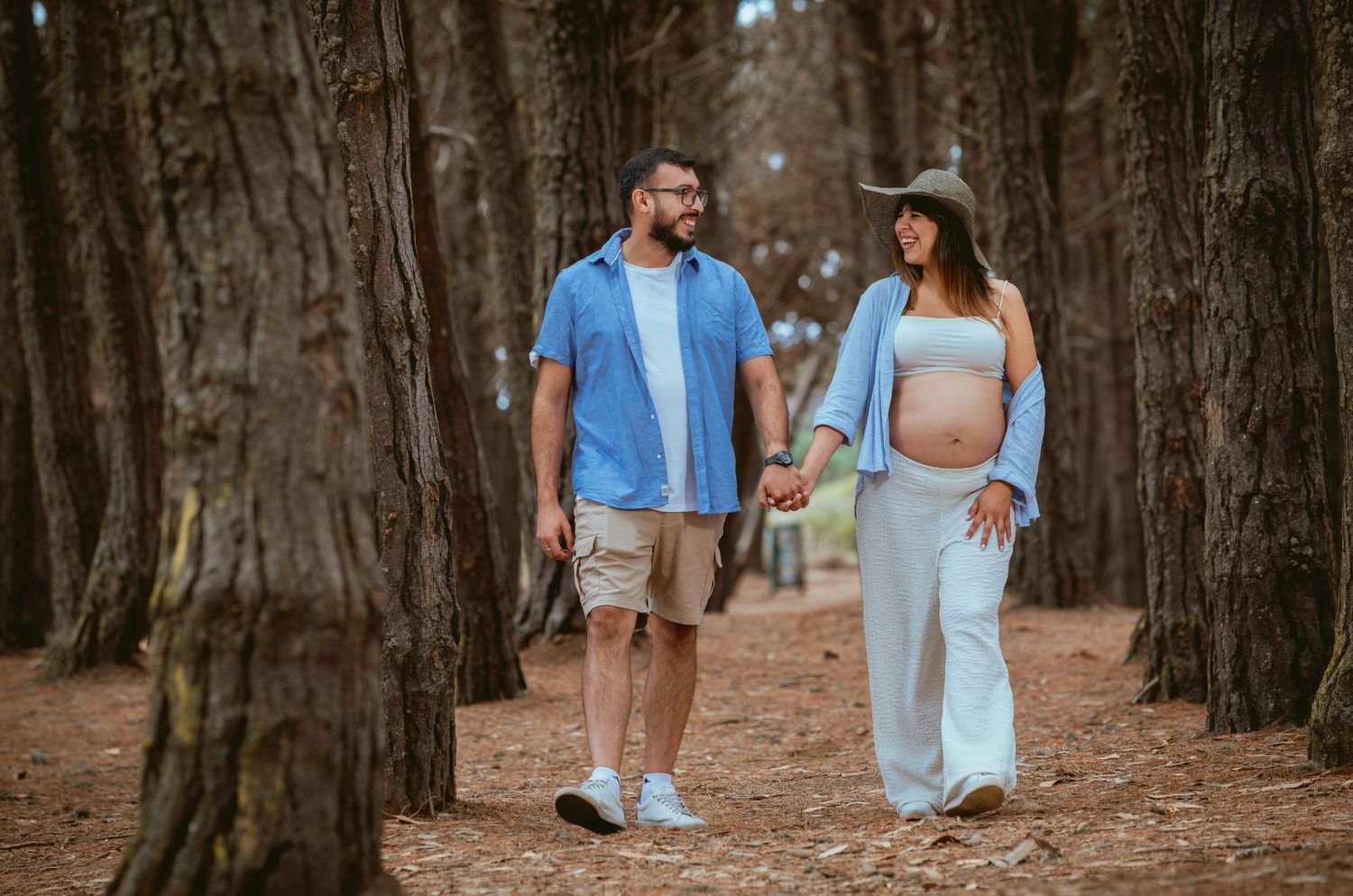 Couple walking hand in hand through pine forest maternity photoshoot.