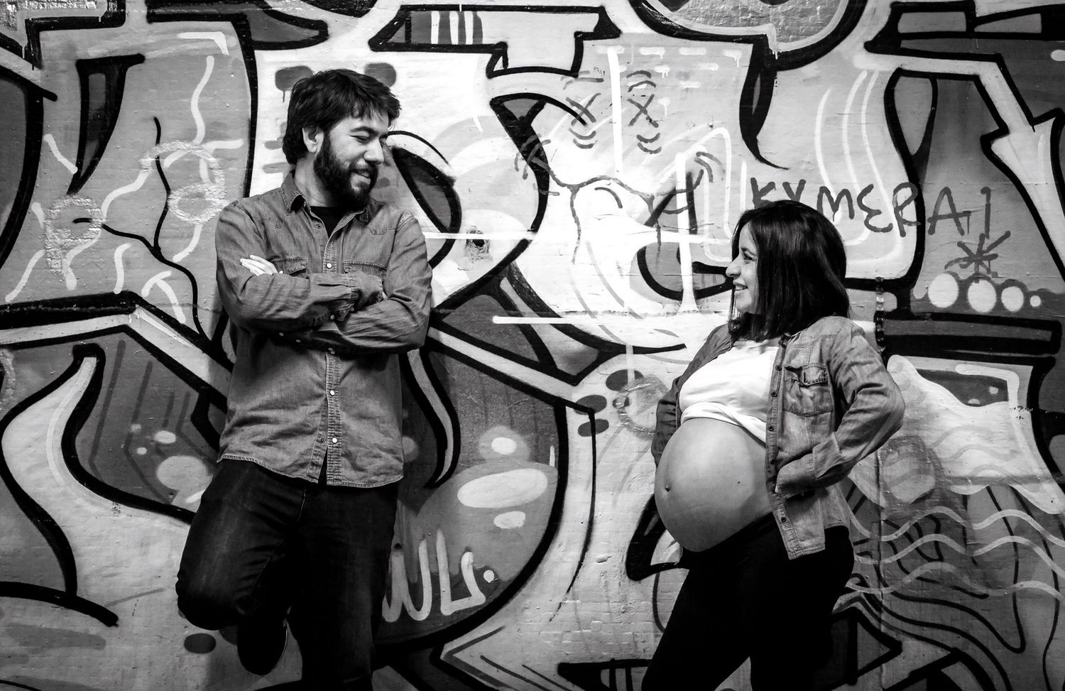 Black and white photo of couple laughing together in front of a graffiti-covered wall.