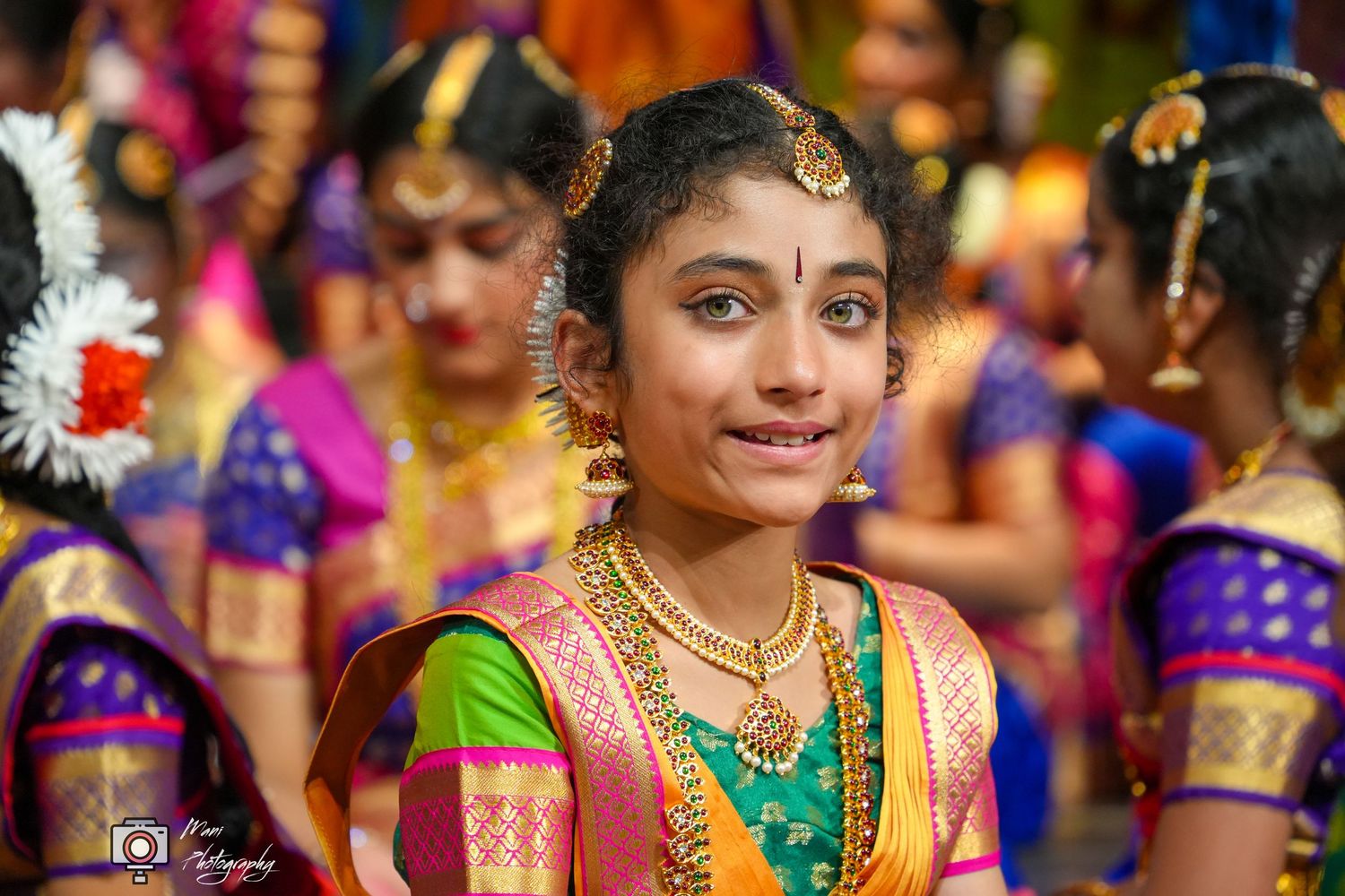 Young Indian girl in traditional Kuchipudi dance attire with gold jewelry and silk saree smiles during cultural performance.