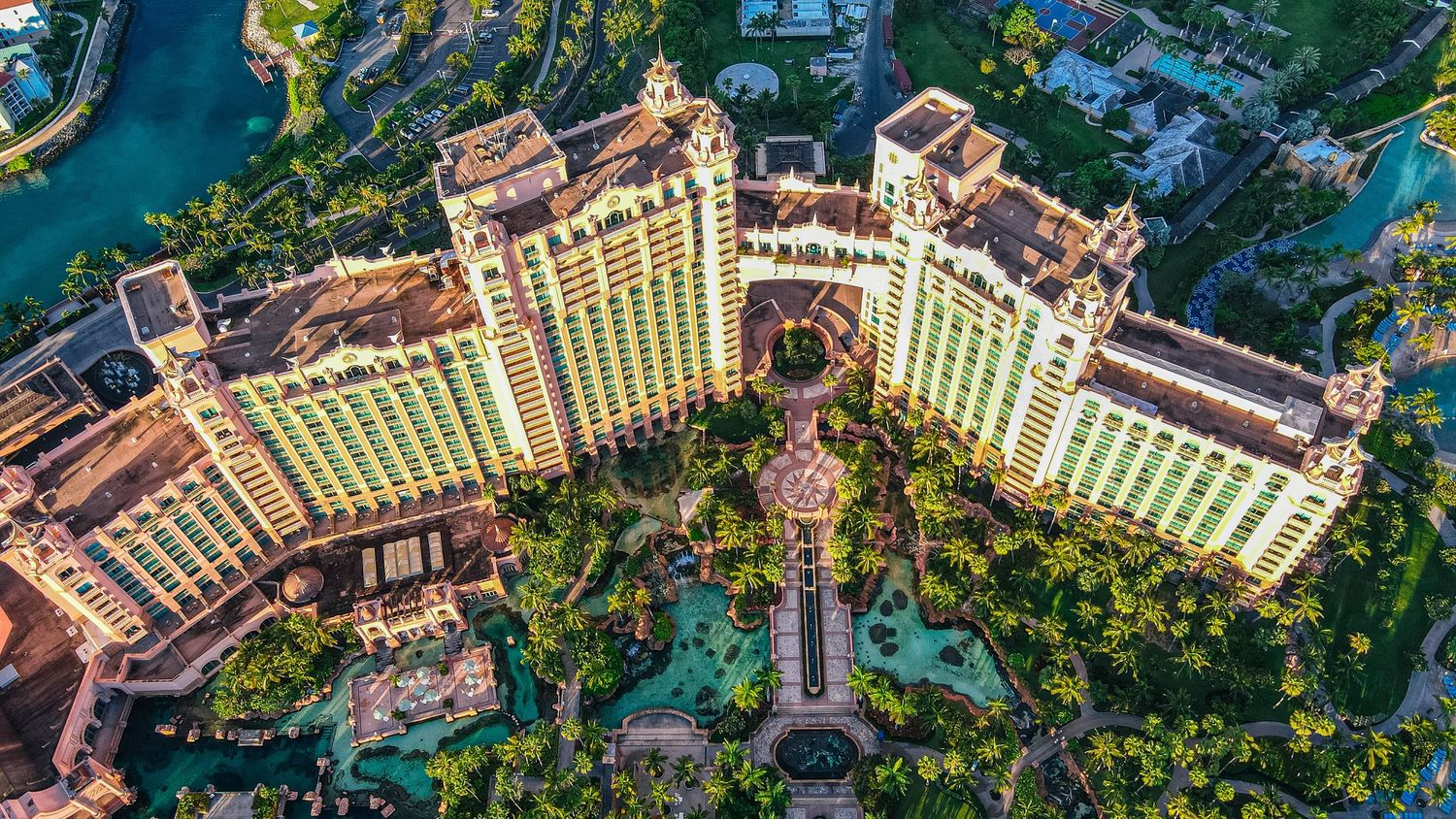 Aerial view of a luxurious resort hotel with golden towers, lush tropical gardens, and sparkling blue pools.