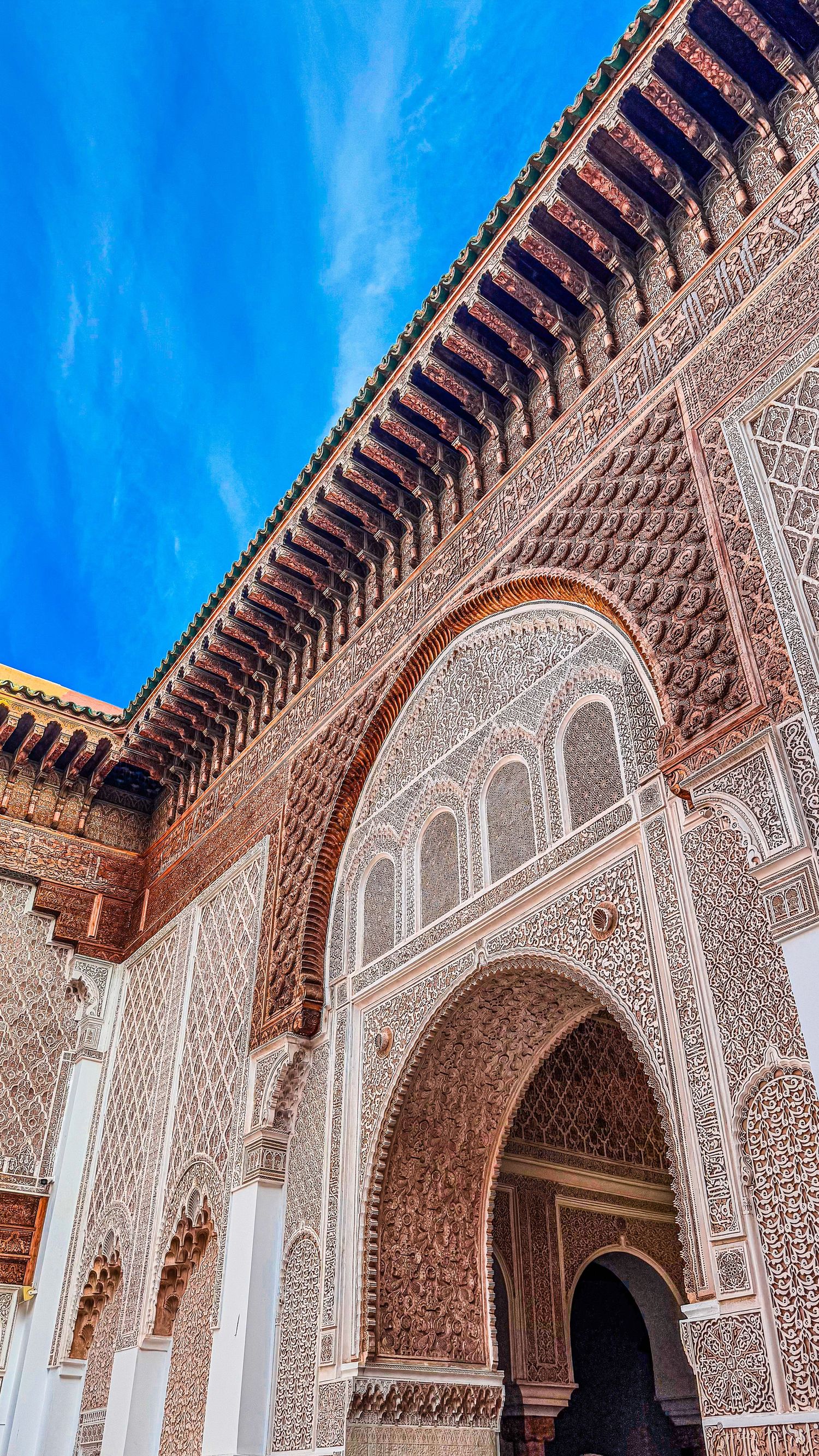 Intricate Moroccan architecture featuring ornate stucco carvings, horseshoe arches, and colorful tilework under a vivid blue sky.