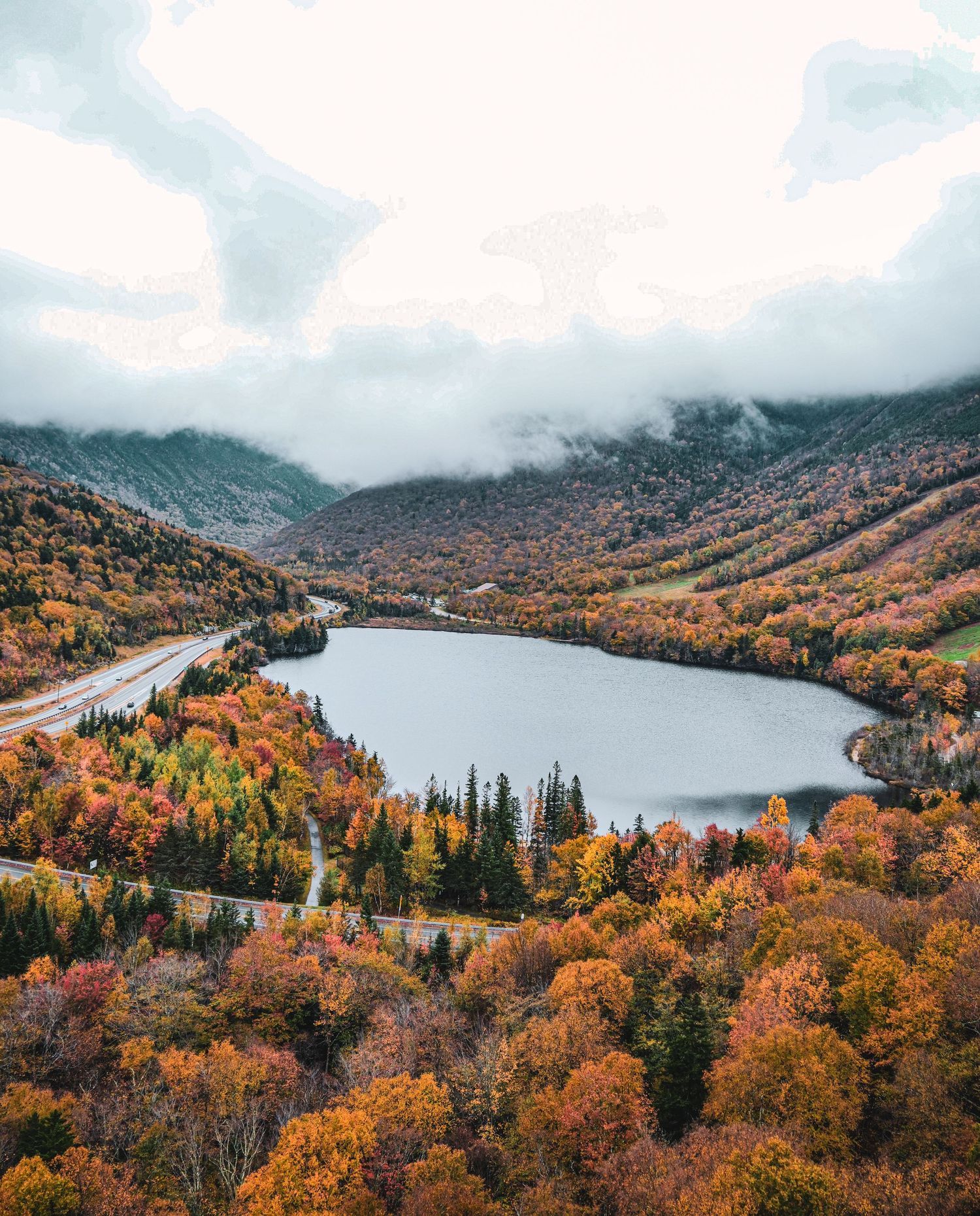 Stunning aerial view of a heart-shaped lake nestled among vibrant autumn mountains under cloudy skies.