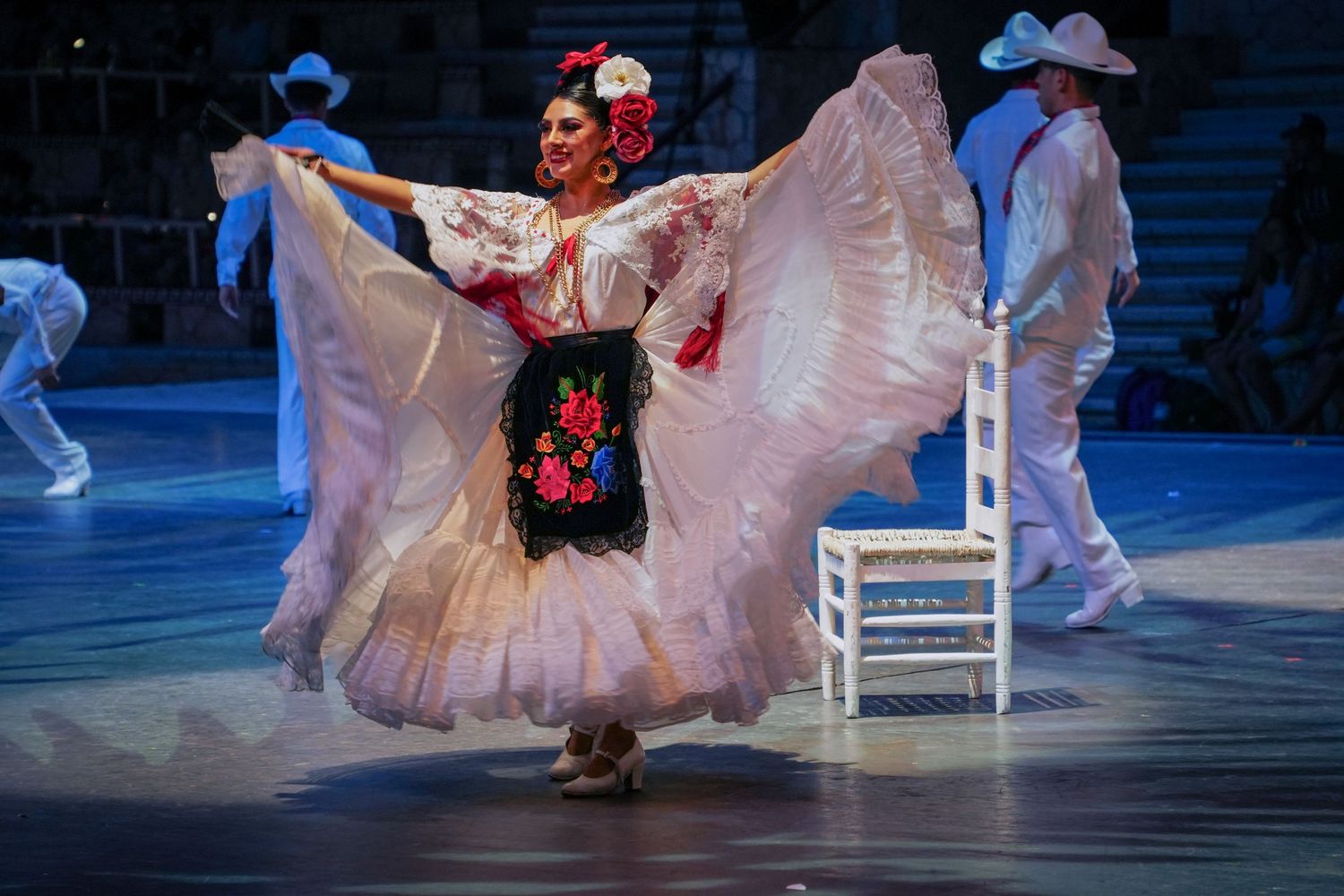 Dancer in traditional Mexican Folklorico costume twirling white and black embroidered skirt on stage.