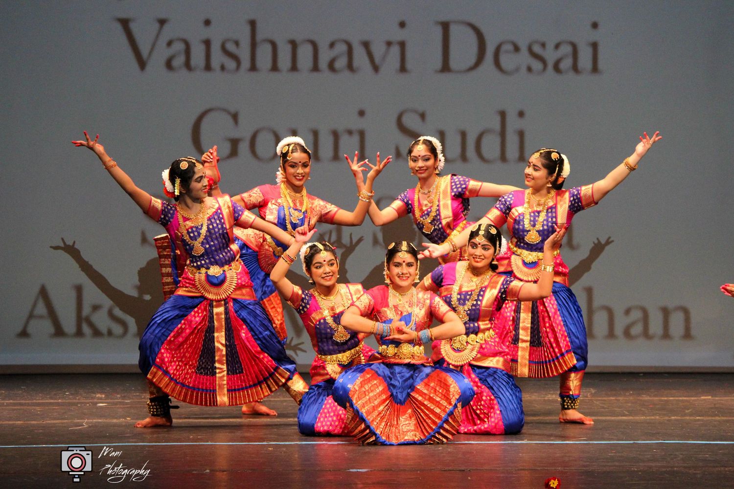 Indian classical dancers in colorful Bharatanatyam costumes perform on stage at a cultural dance recital.