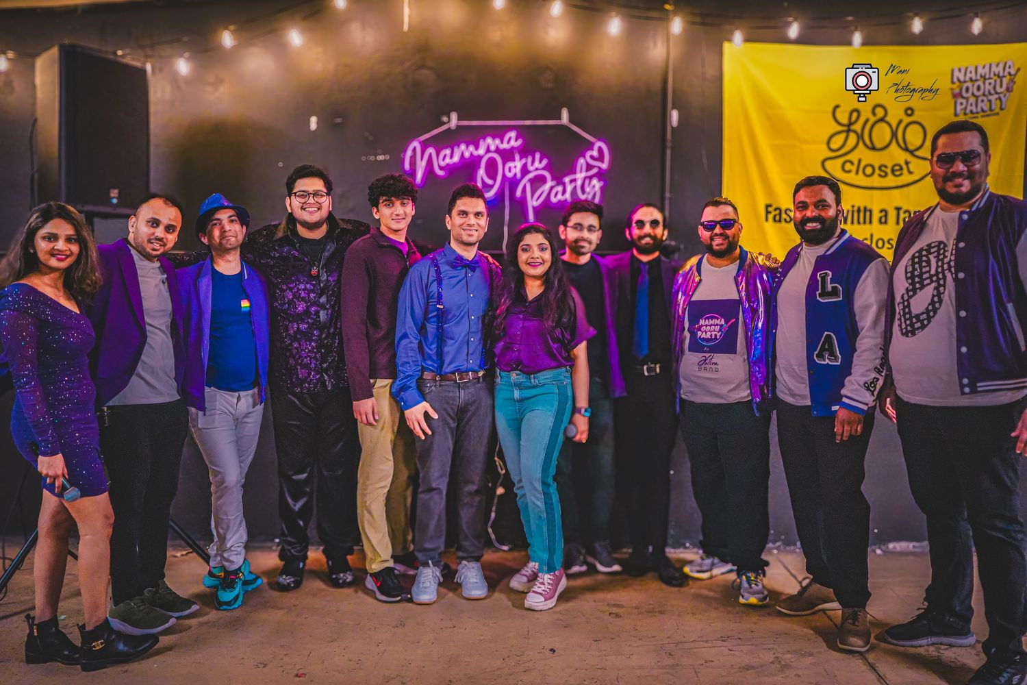 Group of friends posing together at Namma Ooru Party event with neon sign.