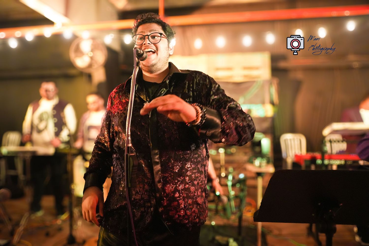 Energetic male singer performing on stage with microphone at a lively indoor music event.