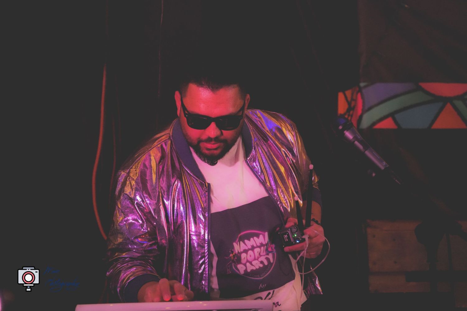 DJ in shiny silver jacket and sunglasses performing at nightclub event.