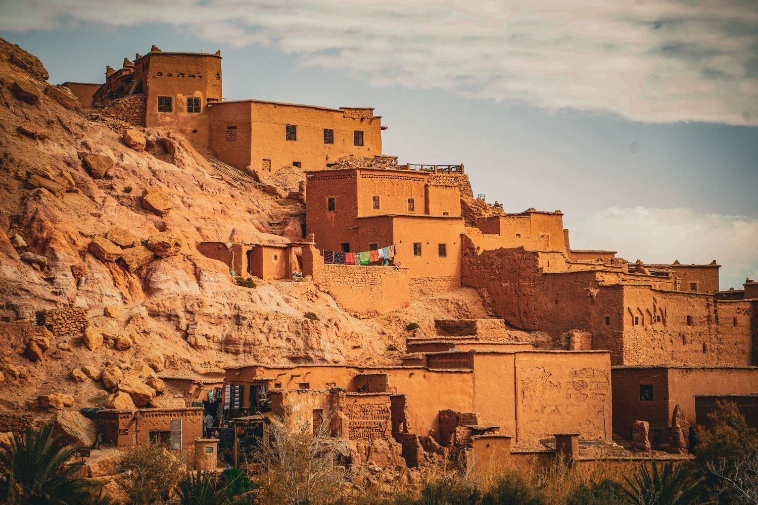 Ancient Moroccan kasbah built into rocky cliffs, featuring traditional mud-brick architecture bathed in warm golden sunset light.