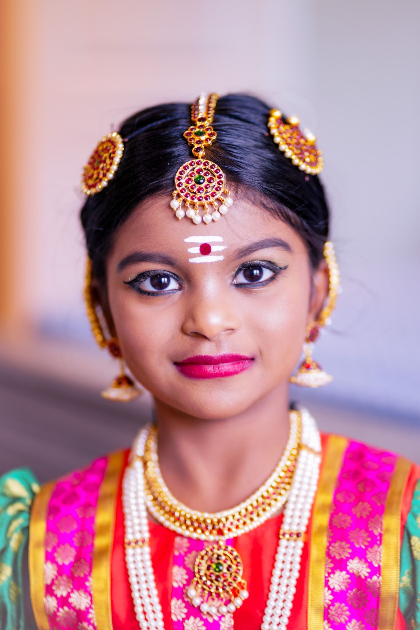Young Indian girl in traditional South Indian bridal attire with gold jewelry and tikka ornament.