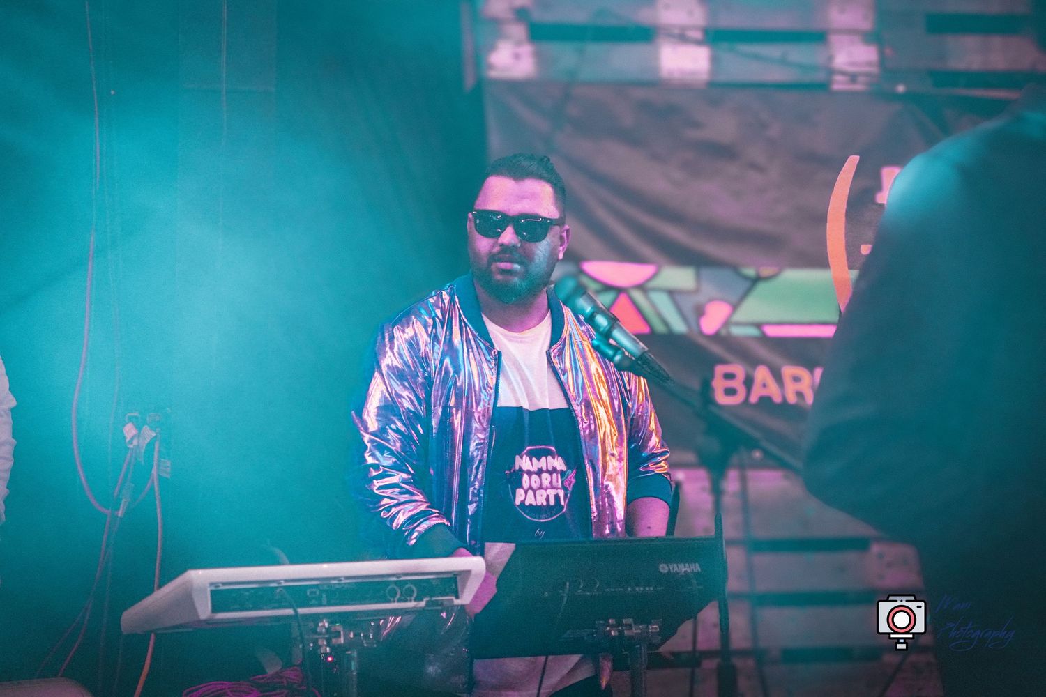 DJ performing at outdoor night event with colorful stage lighting and electronic music equipment.