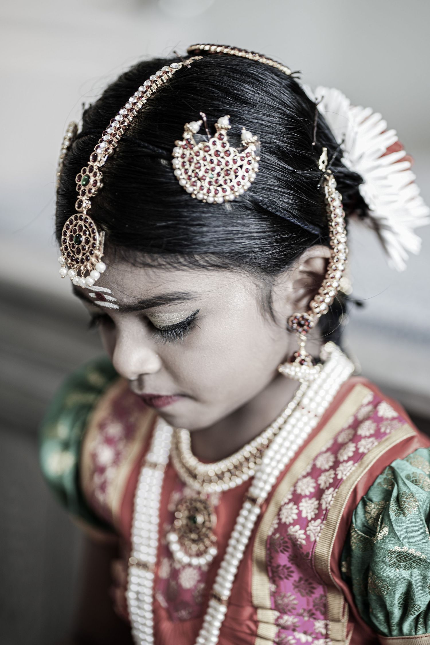 Young Indian girl in traditional South Indian costume adorned with pearl necklaces and gold hair ornaments.