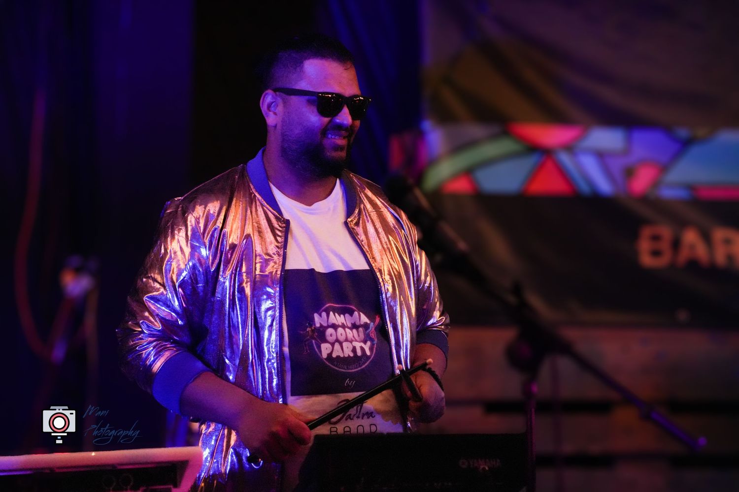Male DJ in metallic purple jacket and sunglasses performing at live music event.