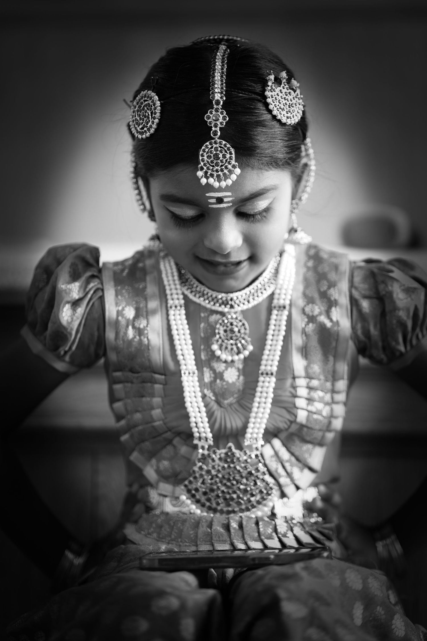 Black and white portrait of a young girl in traditional South Indian jewelry and silk attire at a ceremony.