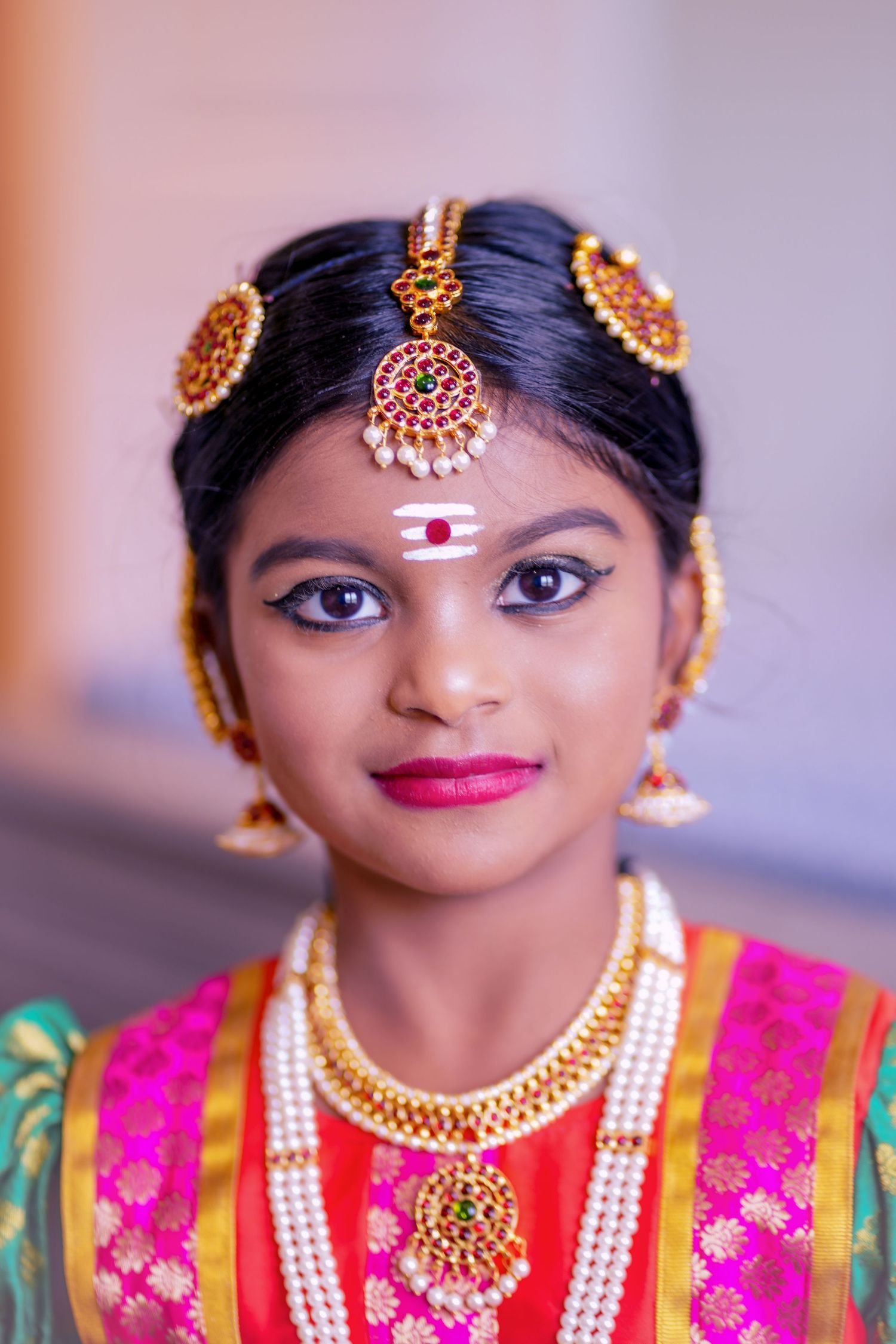 Young Indian girl in traditional South Indian bridal attire with gold jewelry, maang tikka, and vibrant pink saree.