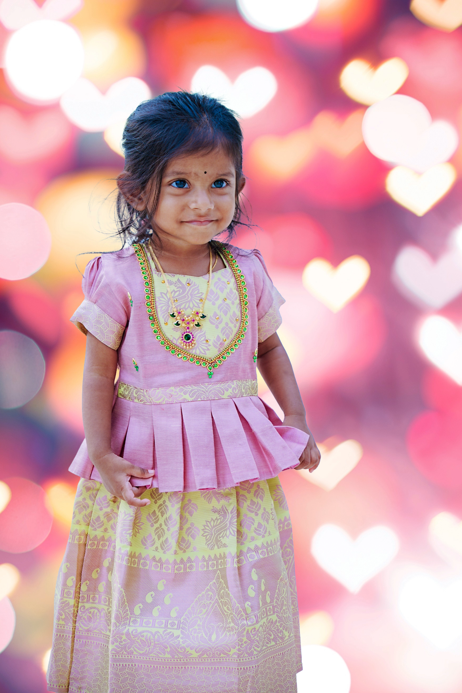 Sweet Indian little girl in pink traditional lehenga with heart-shaped bokeh background.