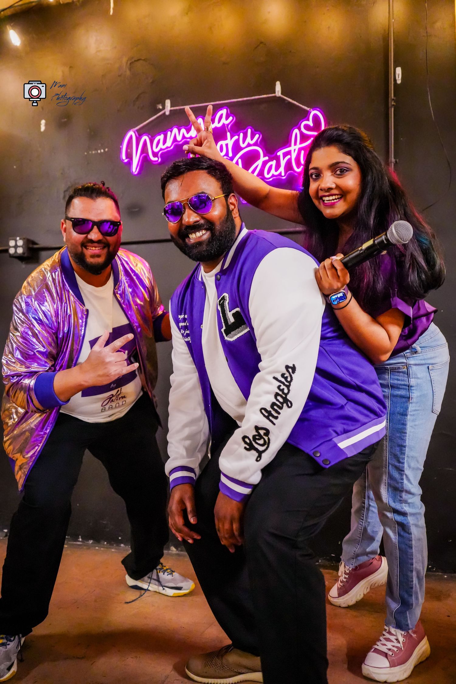 Three friends pose energetically at a neon-lit party venue with microphone and purple accents.