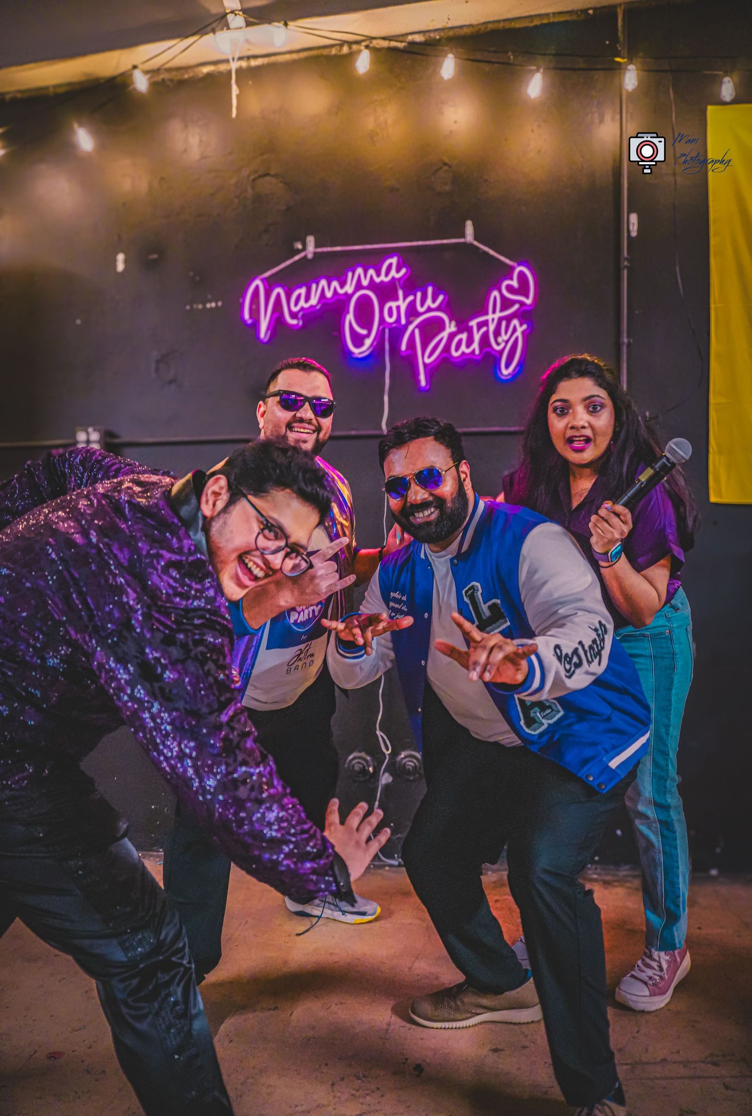 Four friends posing energetically at Namma Ooru Party event with neon sign backdrop.