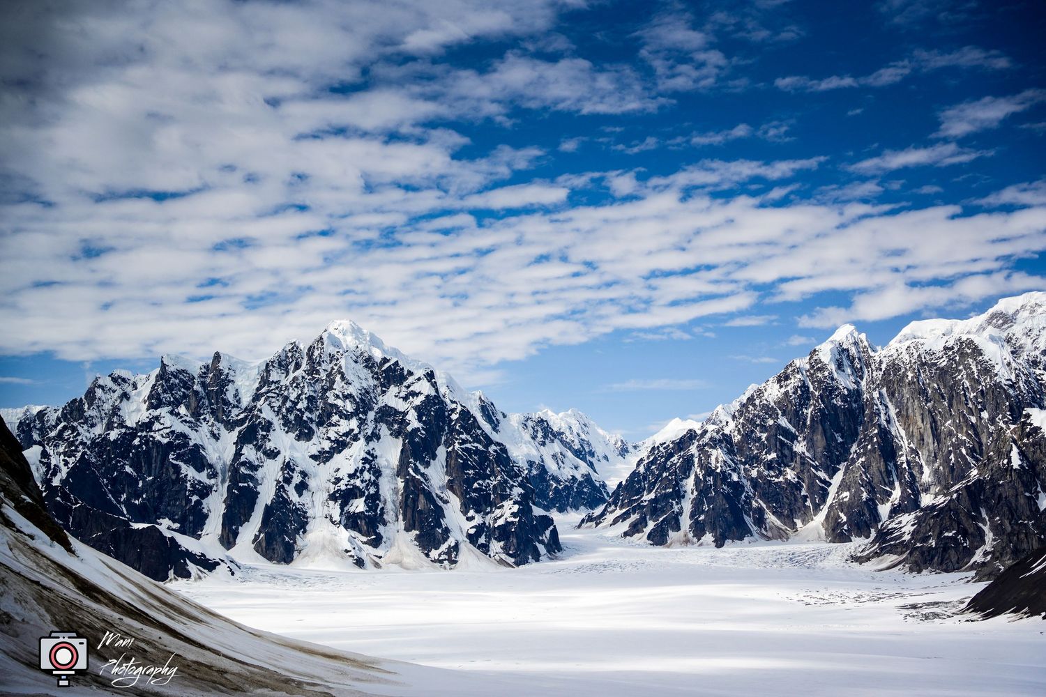 Panoramic view of snow-covered mountain range with glacier under blue sky.