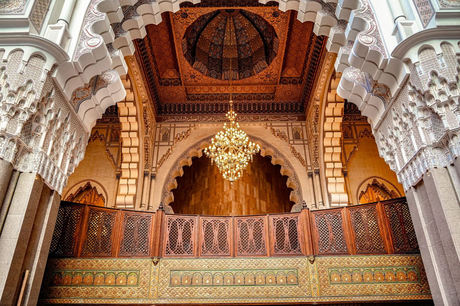 Ornate Moroccan architecture featuring intricate carved details, a gilded chandelier, and a stunning decorative dome ceiling.