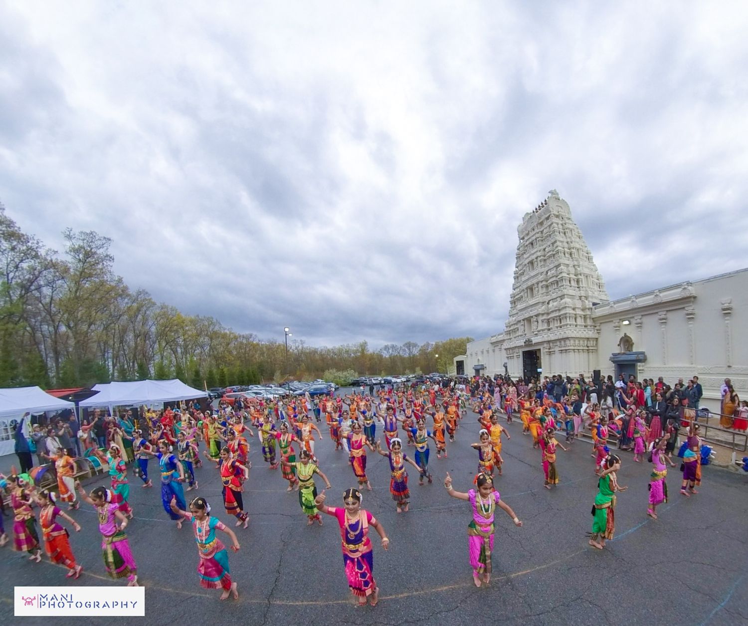 Large crowd of colorful traditional dancers performing outdoors at Hindu temple celebration.