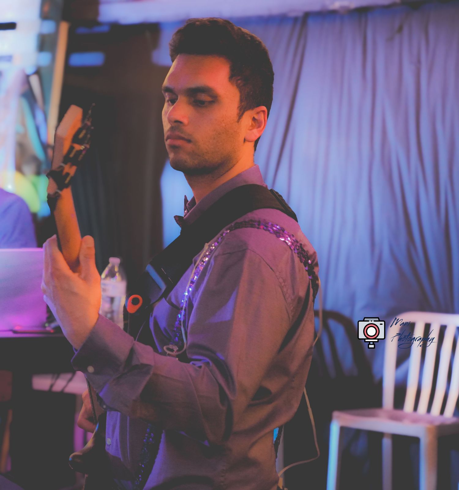 Focused male guitarist playing electric guitar under blue stage lighting at a live concert.