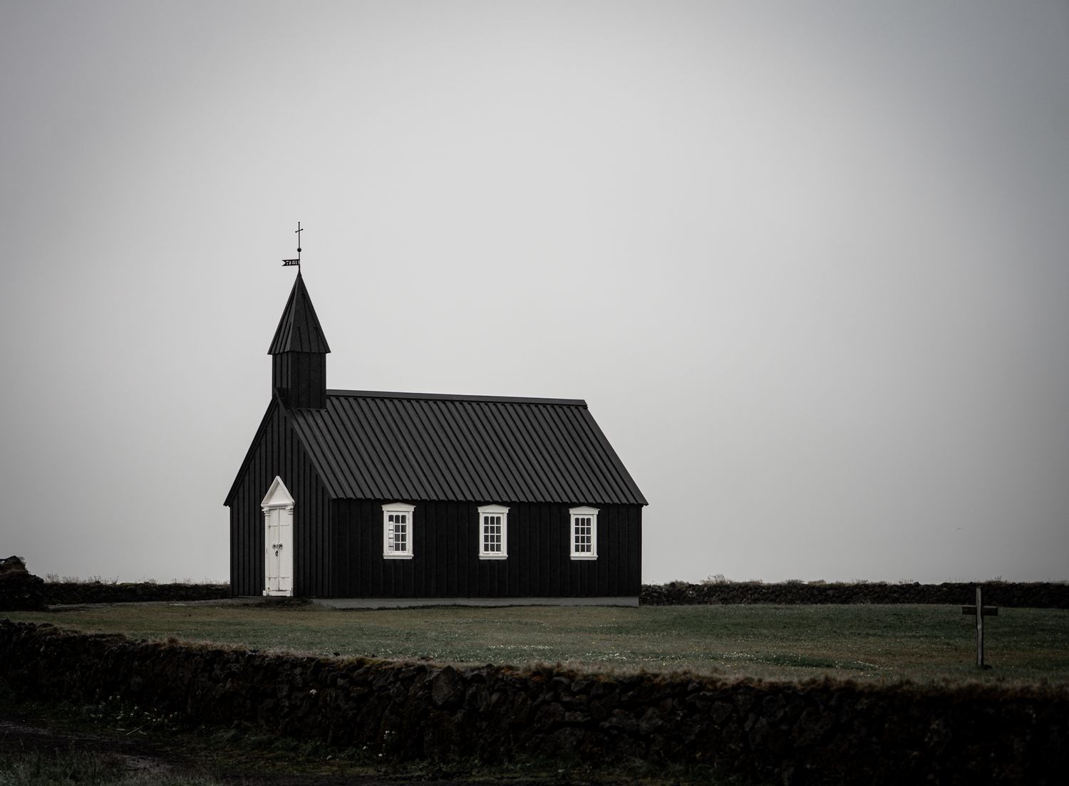 Iconic black Icelandic church with white windows and door standing alone on open landscape.