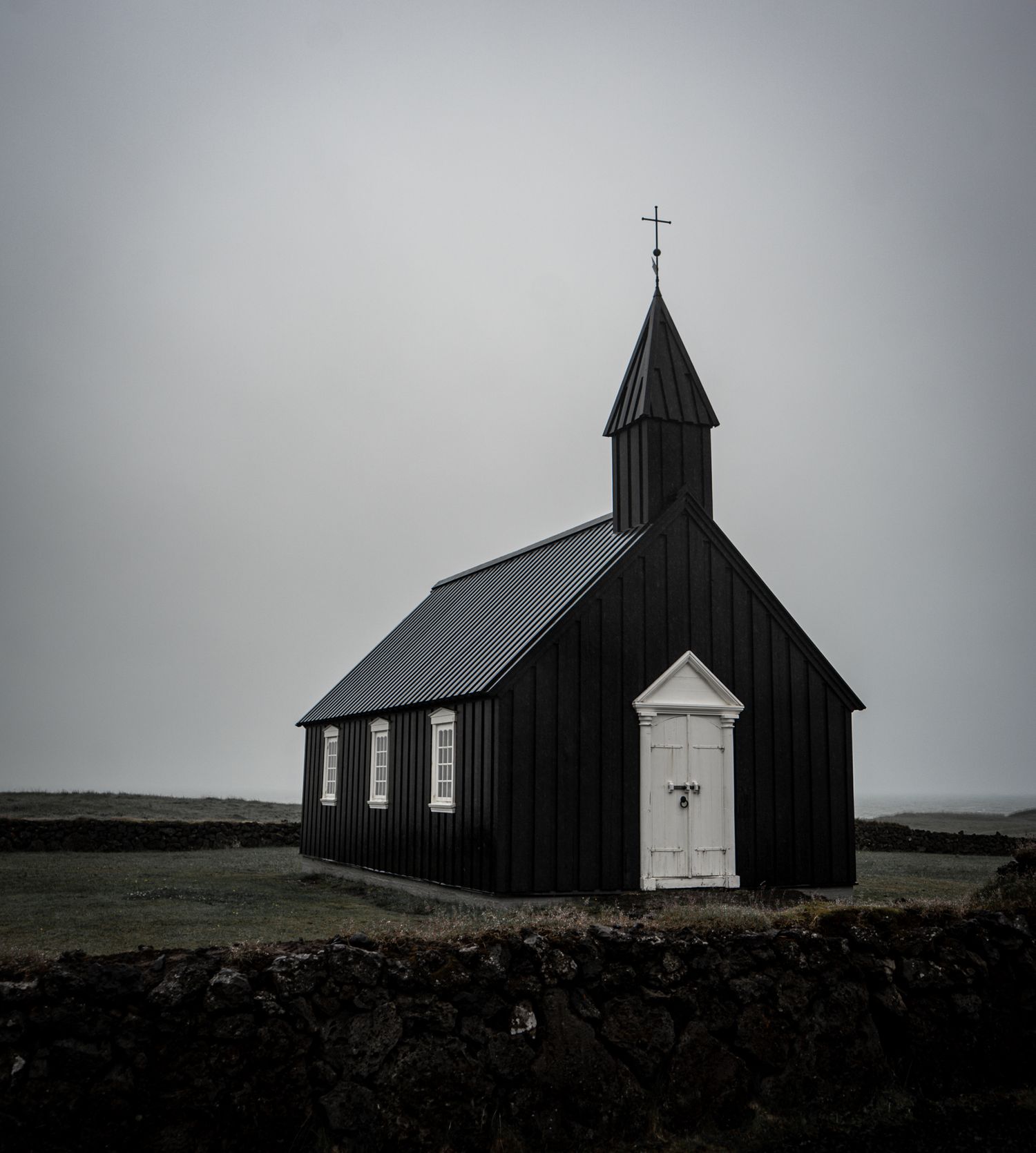Historic black Budir church with white door and cross against overcast sky in Iceland.