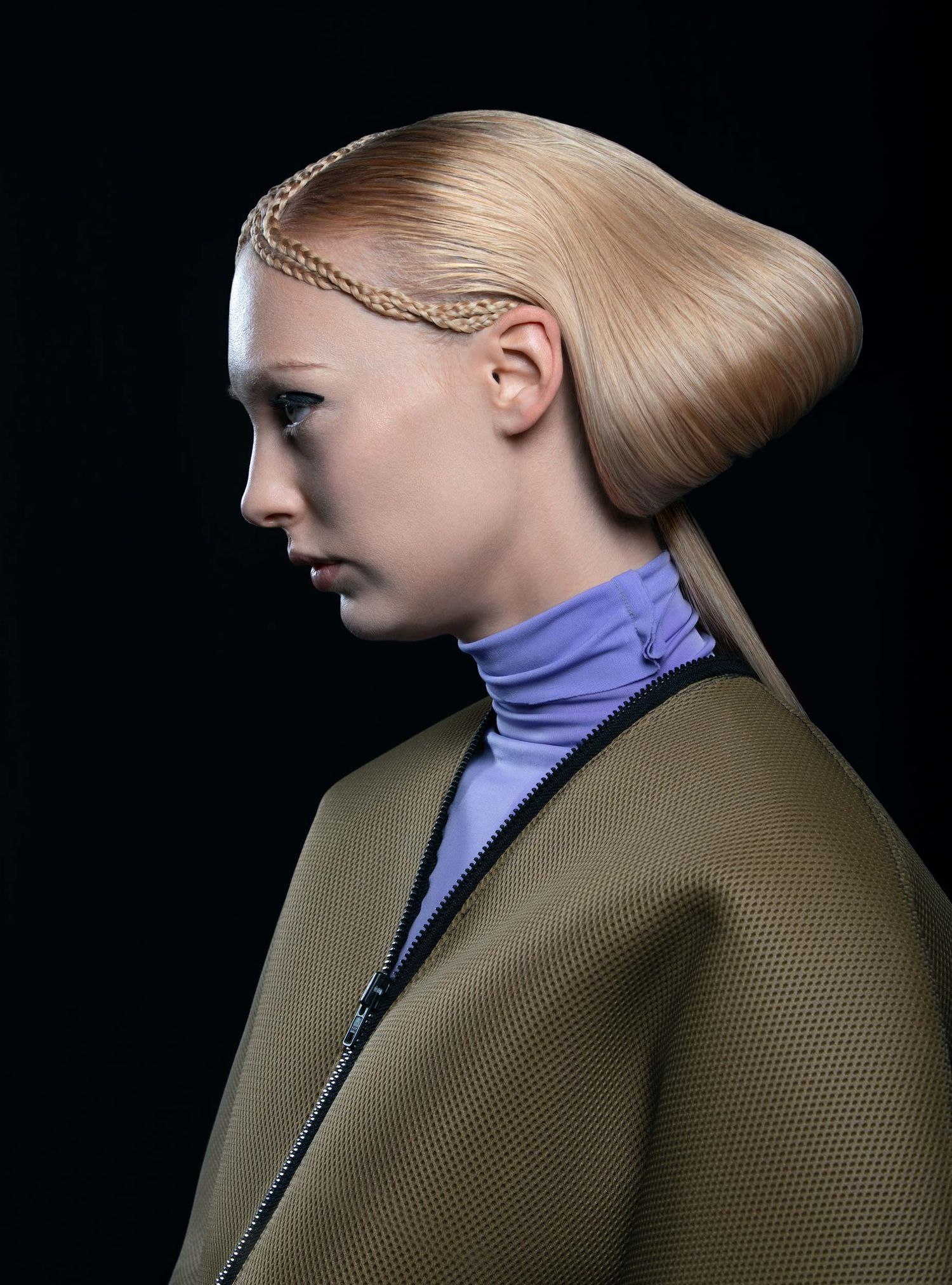 Model with sleek blonde updo hairstyle featuring braided detail, wearing lavender turtleneck and olive jacket, side profile view.