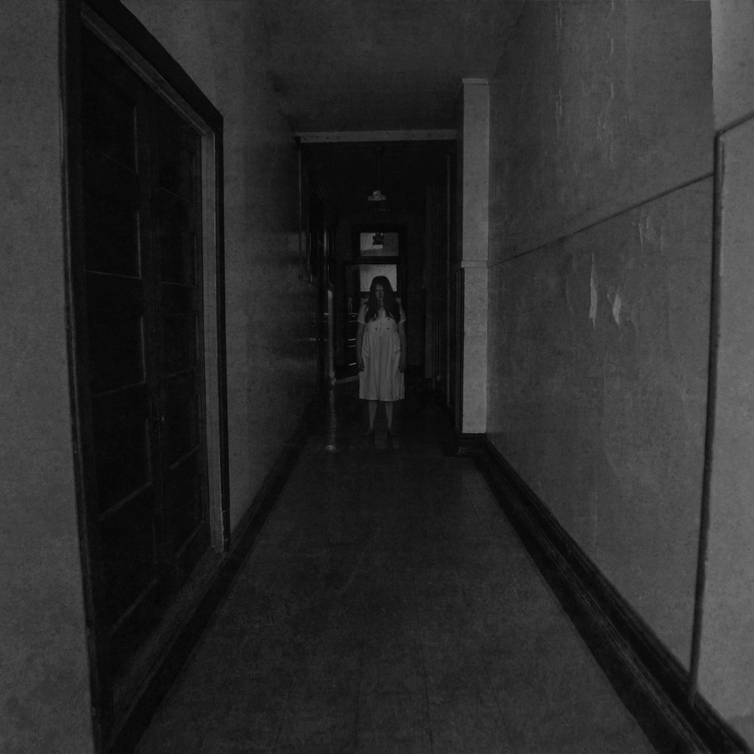 Eerie black and white hallway with ghostly figure of girl in white dress standing in dim corridor.