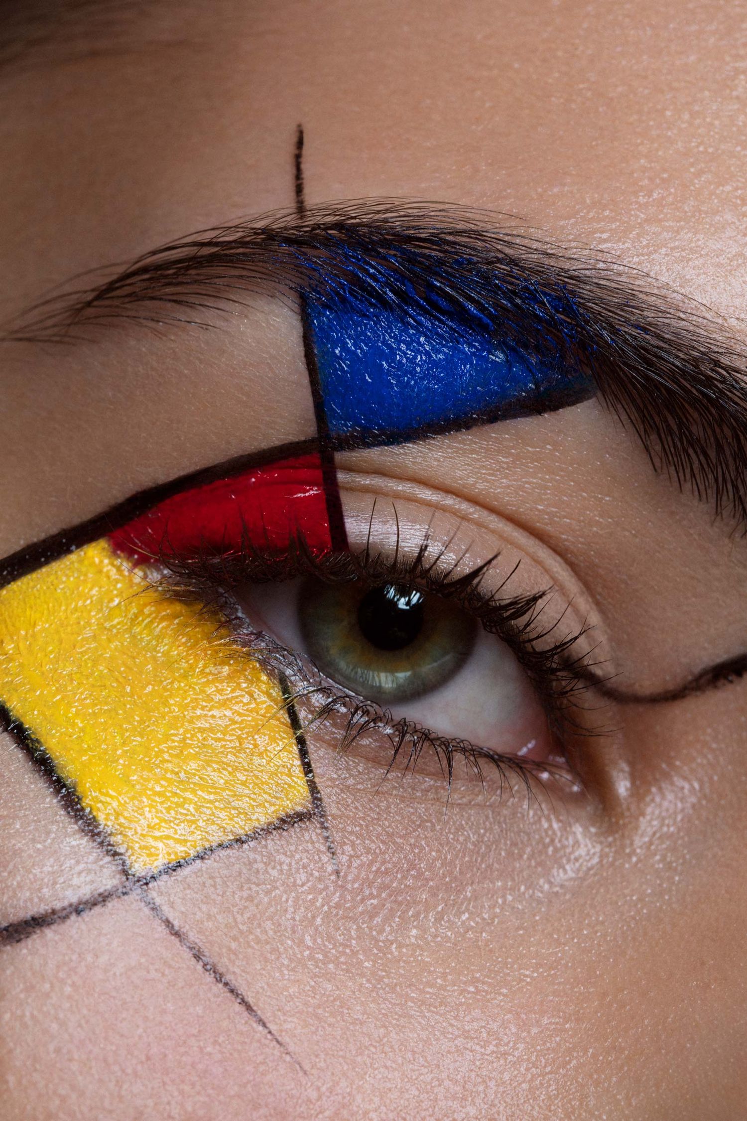 Close-up of artistic Mondrian-inspired eye makeup featuring bold red, blue, and yellow geometric shapes with black lines.
