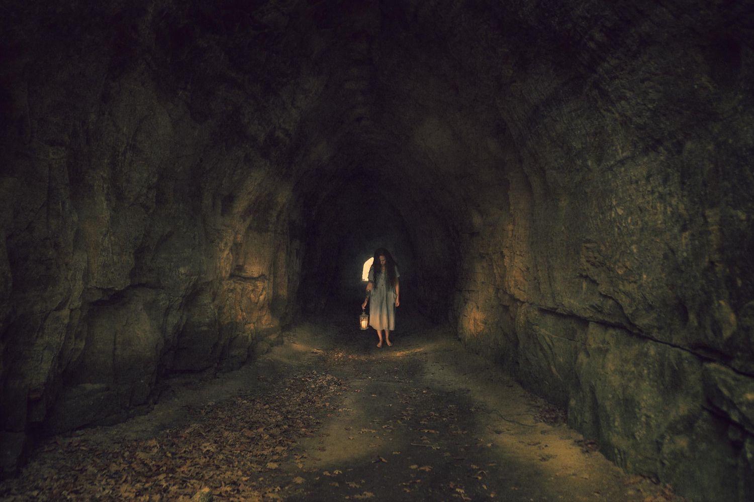 Person walking through a dark, mysterious rock tunnel with dim lighting illuminating the path ahead.
