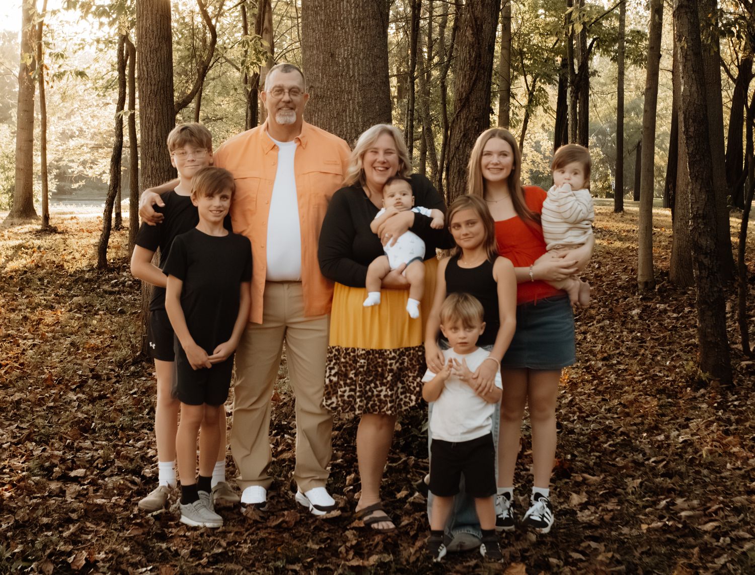 Grandparents posing with five grandchildren of various ages in autumn forest with golden leaves.