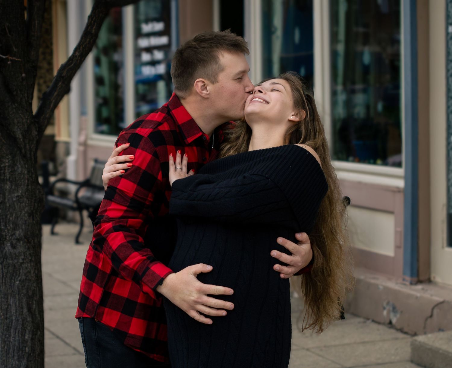 Couple sharing a romantic kiss outdoors on a city sidewalk during an engagement photo session.