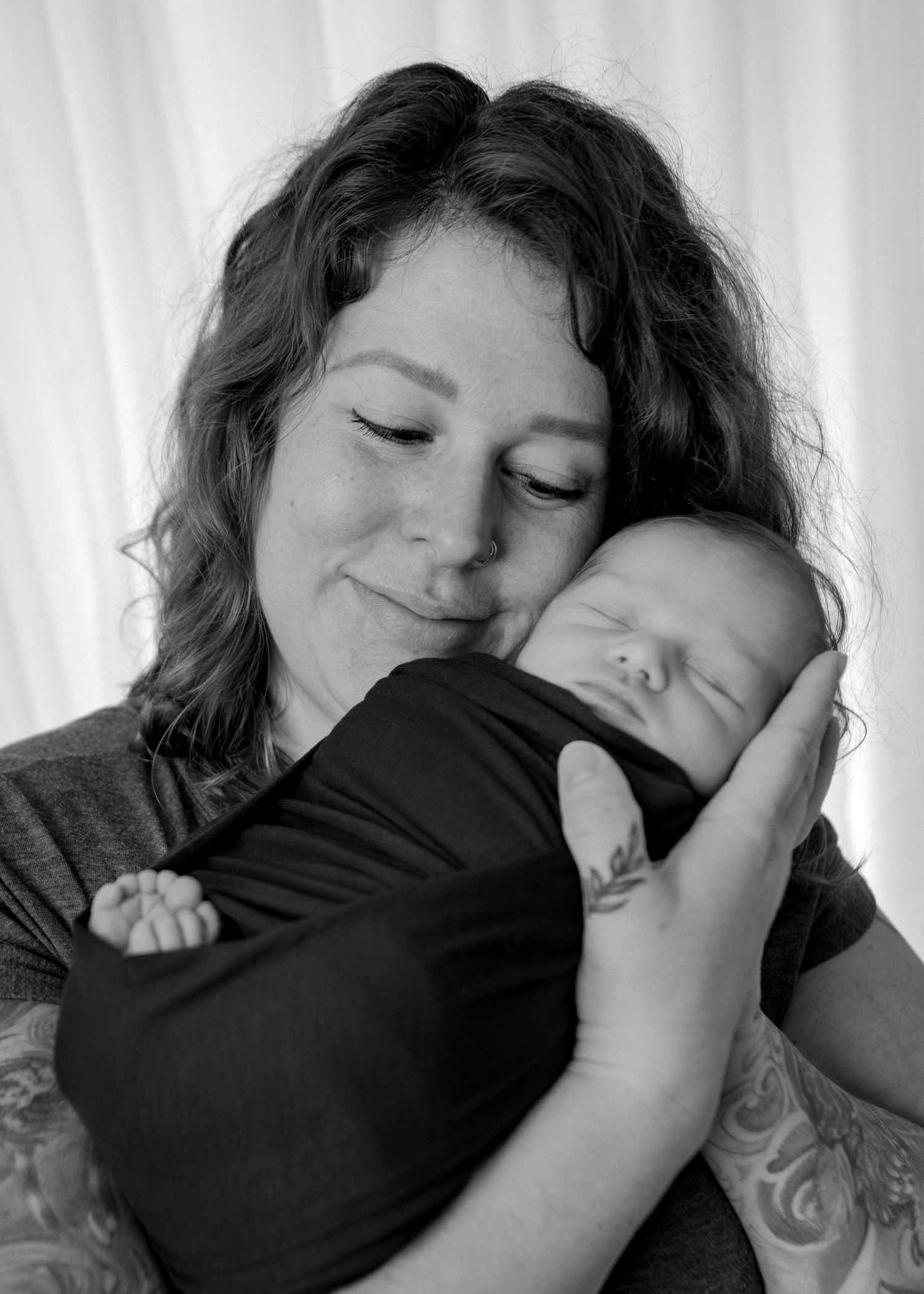 Black and white portrait of a curly-haired mother tenderly holding her sleeping newborn baby.