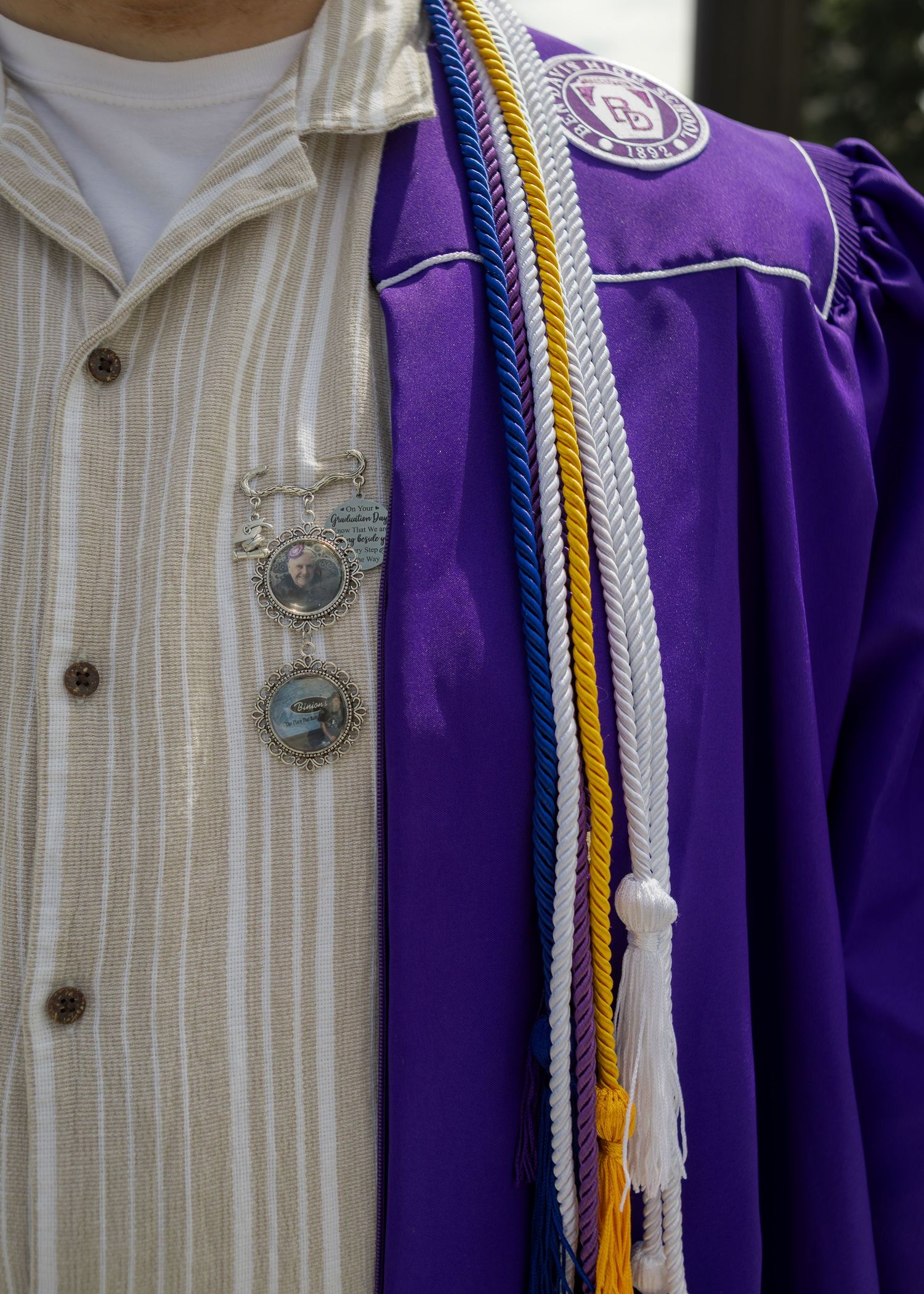 Close-up of purple graduation gown with honor cords in gold, white, and blue with memorial pins.
