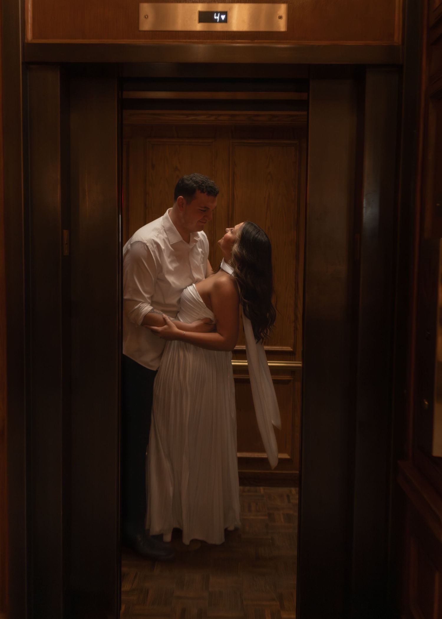 Bride and groom sharing a kiss inside a vintage elevator with wooden doors.